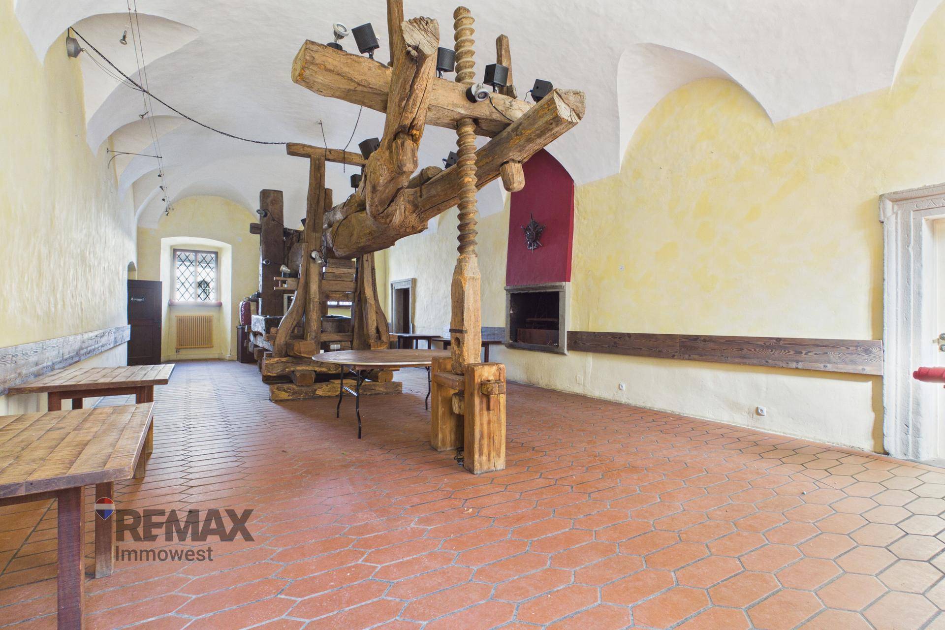 Großer Raum mit historischer Holzpresse als Dekoration und Terrakotta-Boden.