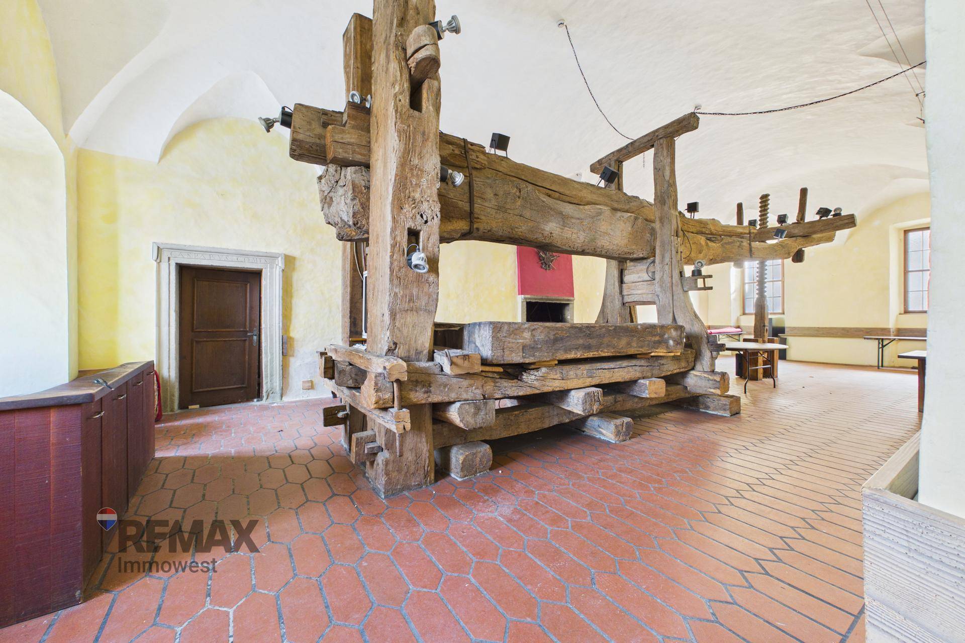 Detailansicht einer massiven historischen Holzpresse in einem großen Raum mit Terrakotta-Boden.