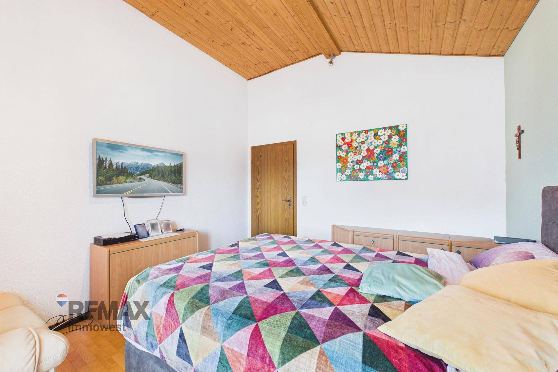 Helles Schlafzimmer mit Holzdachschräge, Parkettboden und farbenfroher Bettdecke, einladend und gemütlich.
