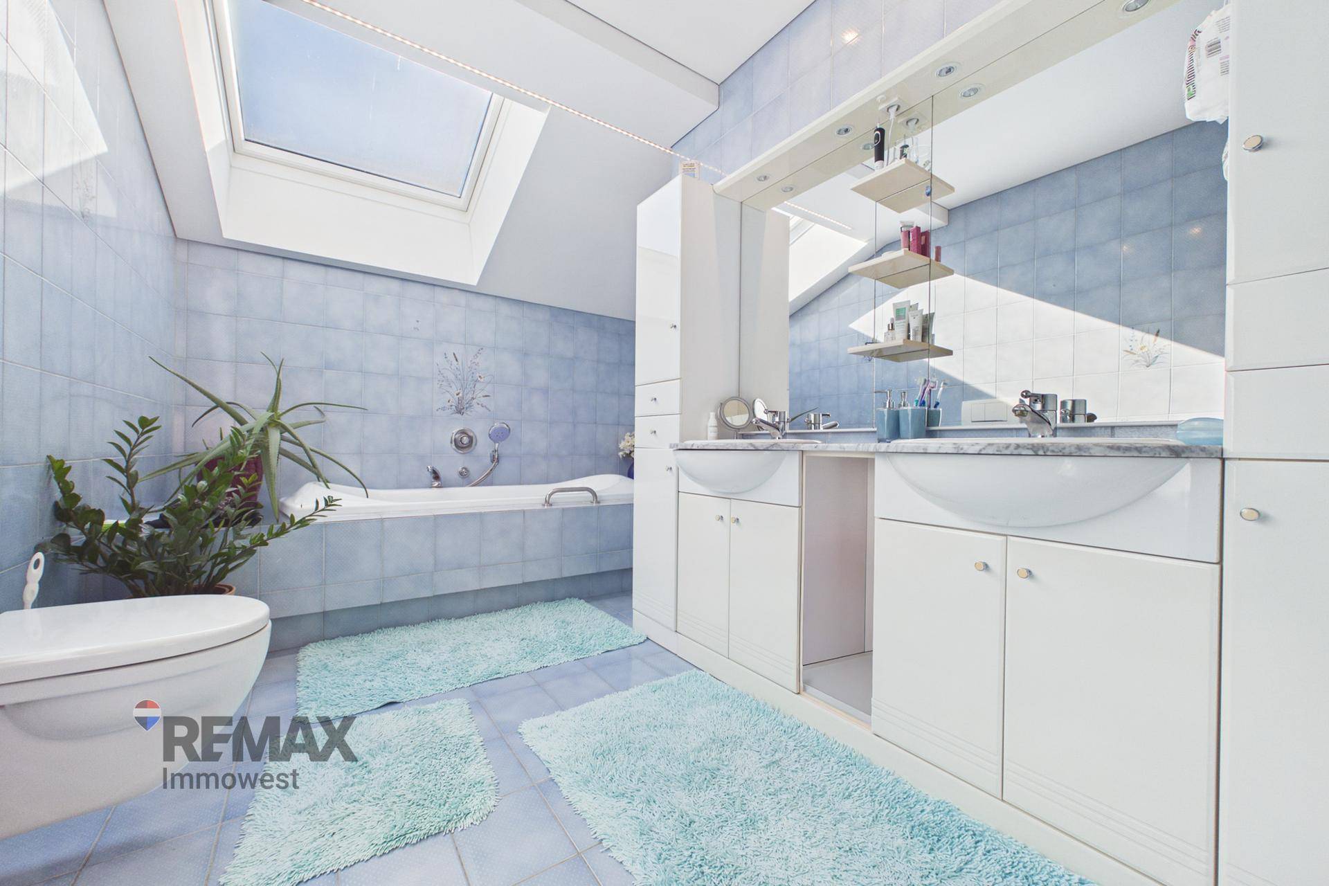 Helles Badezimmer mit blauen Fliesen, Dachfenster und Doppelwaschbecken, gut gepflegt und funktional.