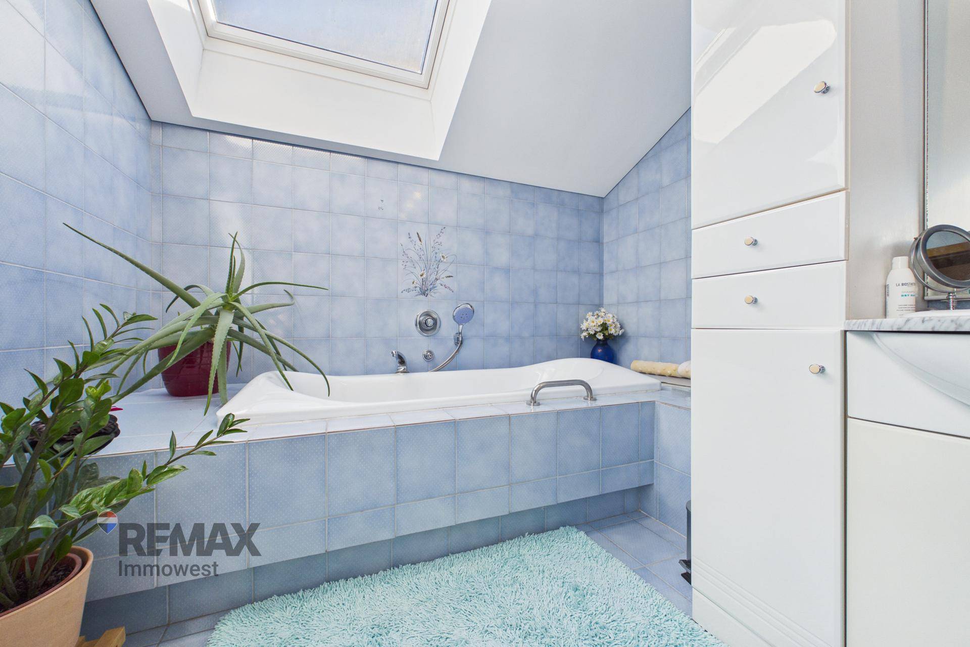 Badezimmer mit blauen Fliesen, Badewanne und Dachfenster für natürliches Licht, einladend und sauber.