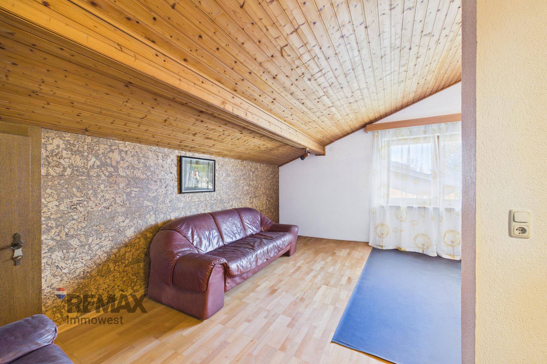 Gemütlicher Raum mit Holzdachschräge, Parkettboden und Ledersofa, ideal als Gästezimmer oder Hobbyraum.