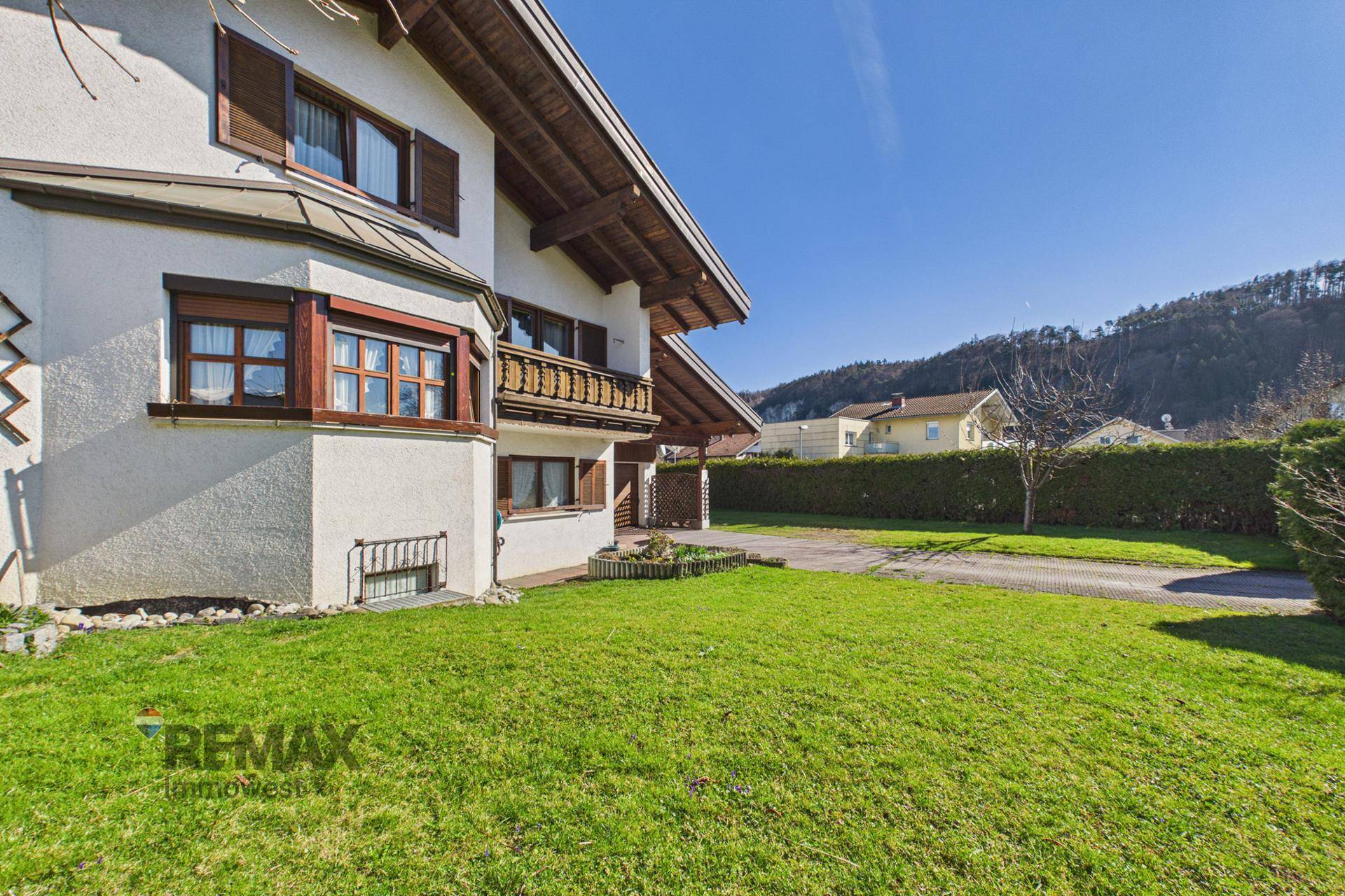 Seitlicher Gartenbereich mit Rasen, Hecke und Blick auf die umliegende Landschaft, sonnig und weitläufig.