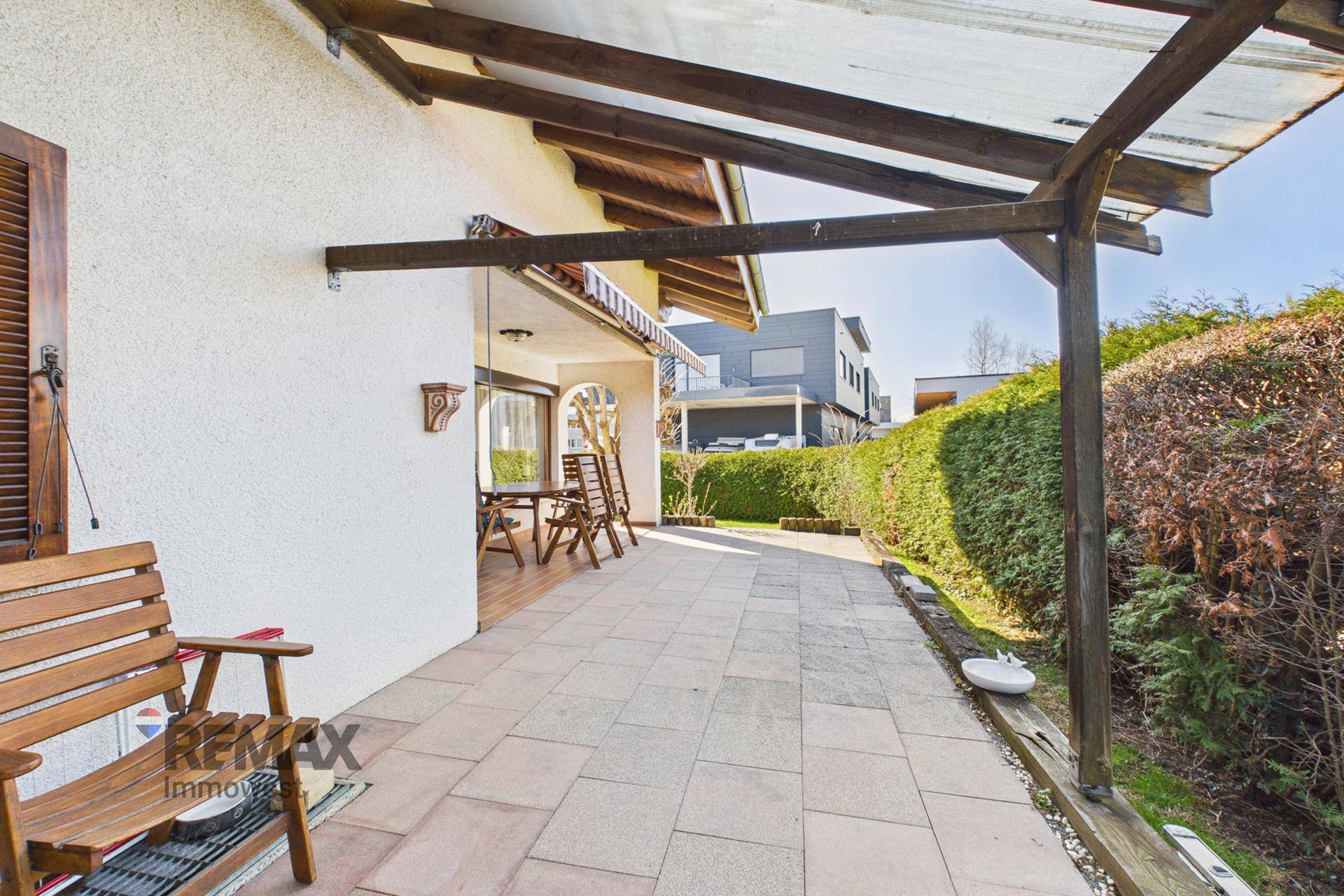 Lange, gepflasterte Terrasse mit Überdachung und Zugang zum Garten, bietet viel Platz im Freien.