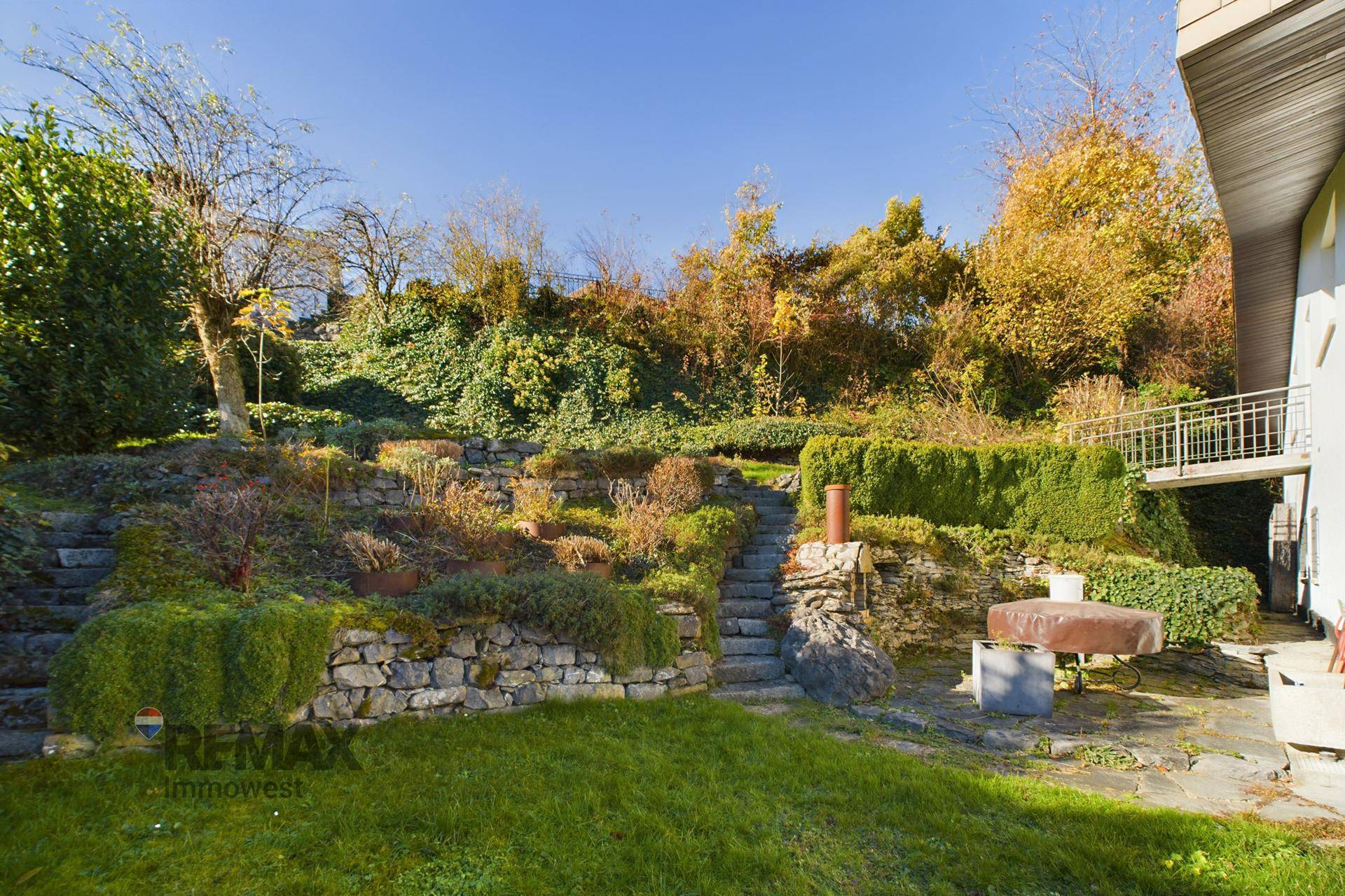 Gestufter Gartenbereich mit Steinmauern, Treppen und üppiger Vegetation unter strahlend blauem Himmel.