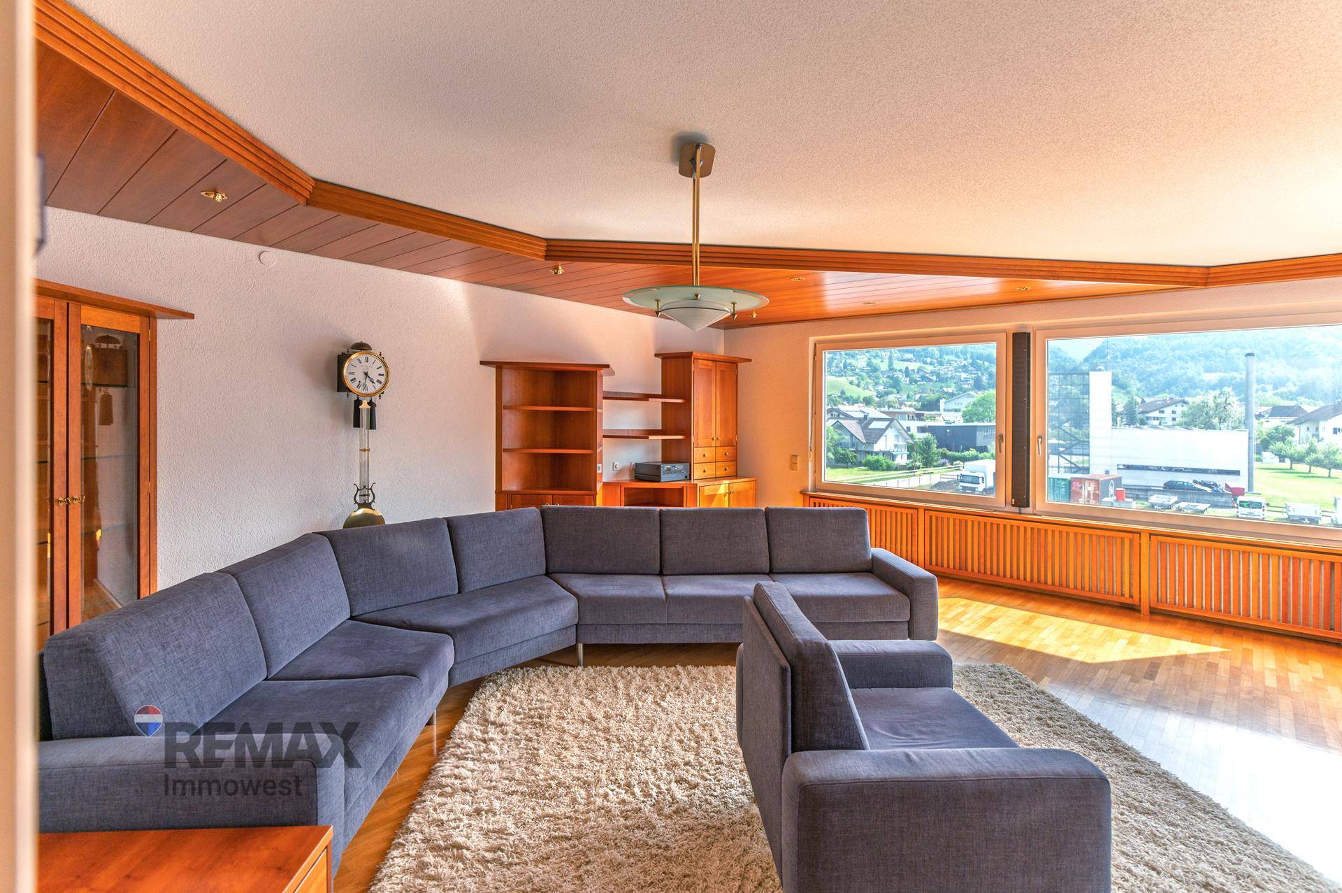 Geräumiges Wohnzimmer mit großer Eckcouch, Holzvertäfelung und weitem Blick durch Panoramafenster.