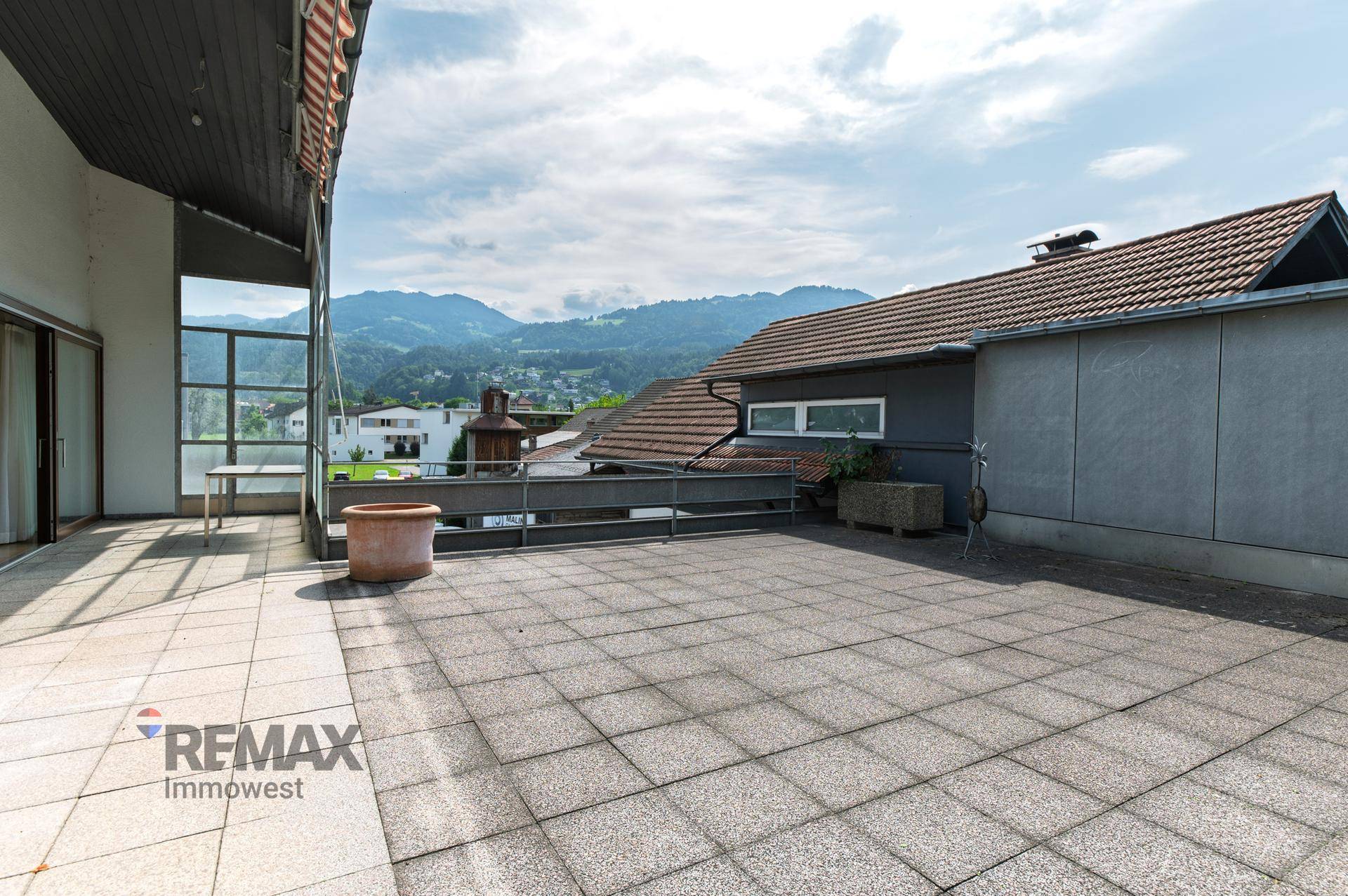 Große geflieste Dachterrasse mit Bergblick und viel Platz für Outdoor-Möbel unter blauem Himmel.