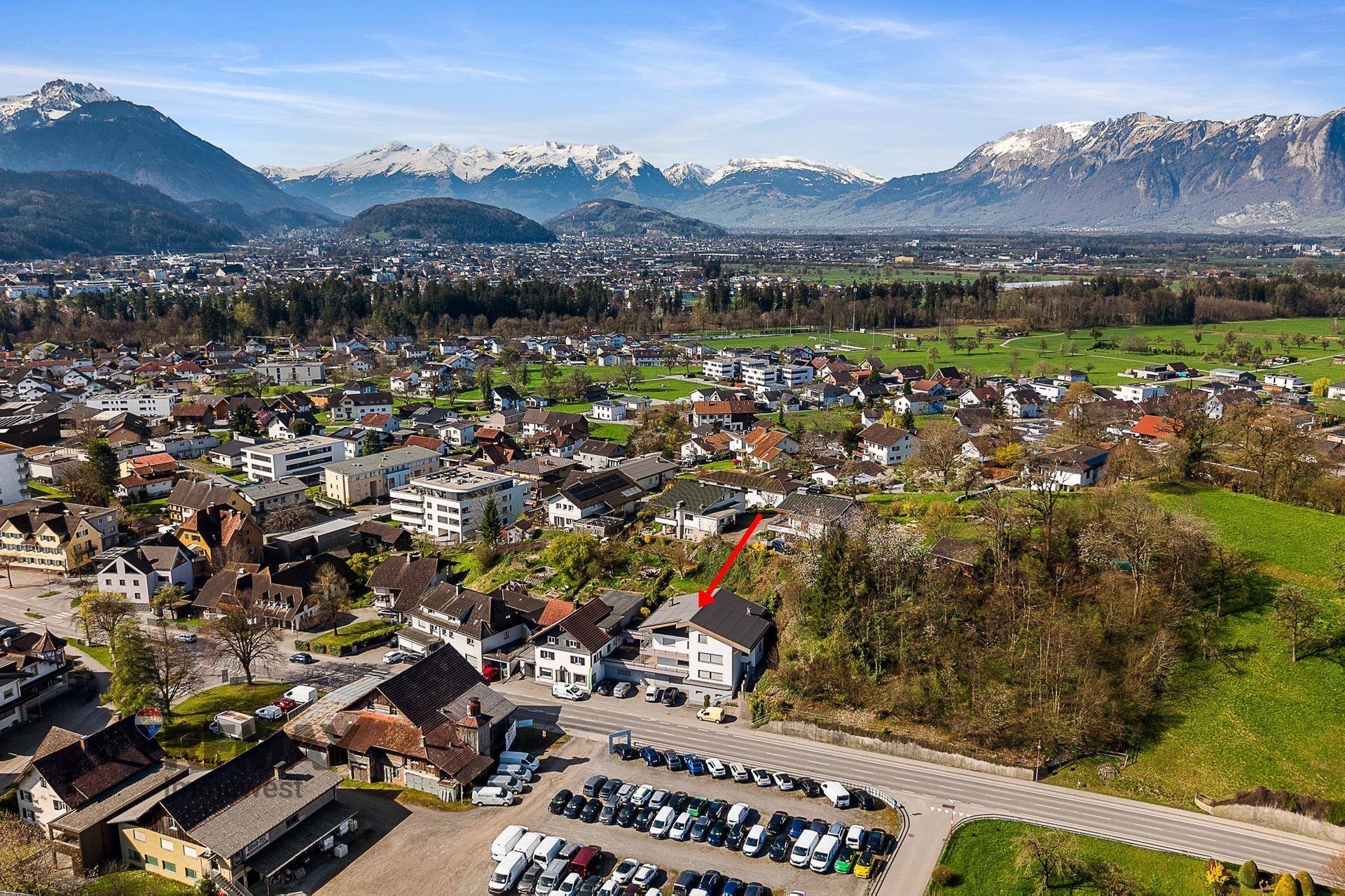 Weitläufige Luftaufnahme einer Stadt mit schneebedeckten Bergen im Hintergrund und einem markierten Gebäude.