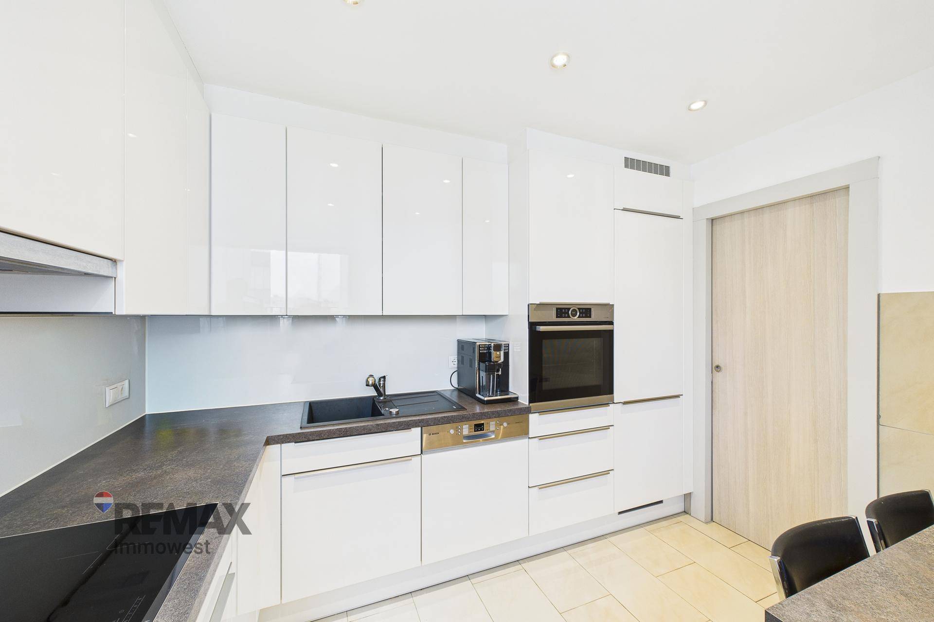 Moderne Einbauküche mit weißen Hochglanzschränken, dunkler Arbeitsplatte und integrierten Geräten.