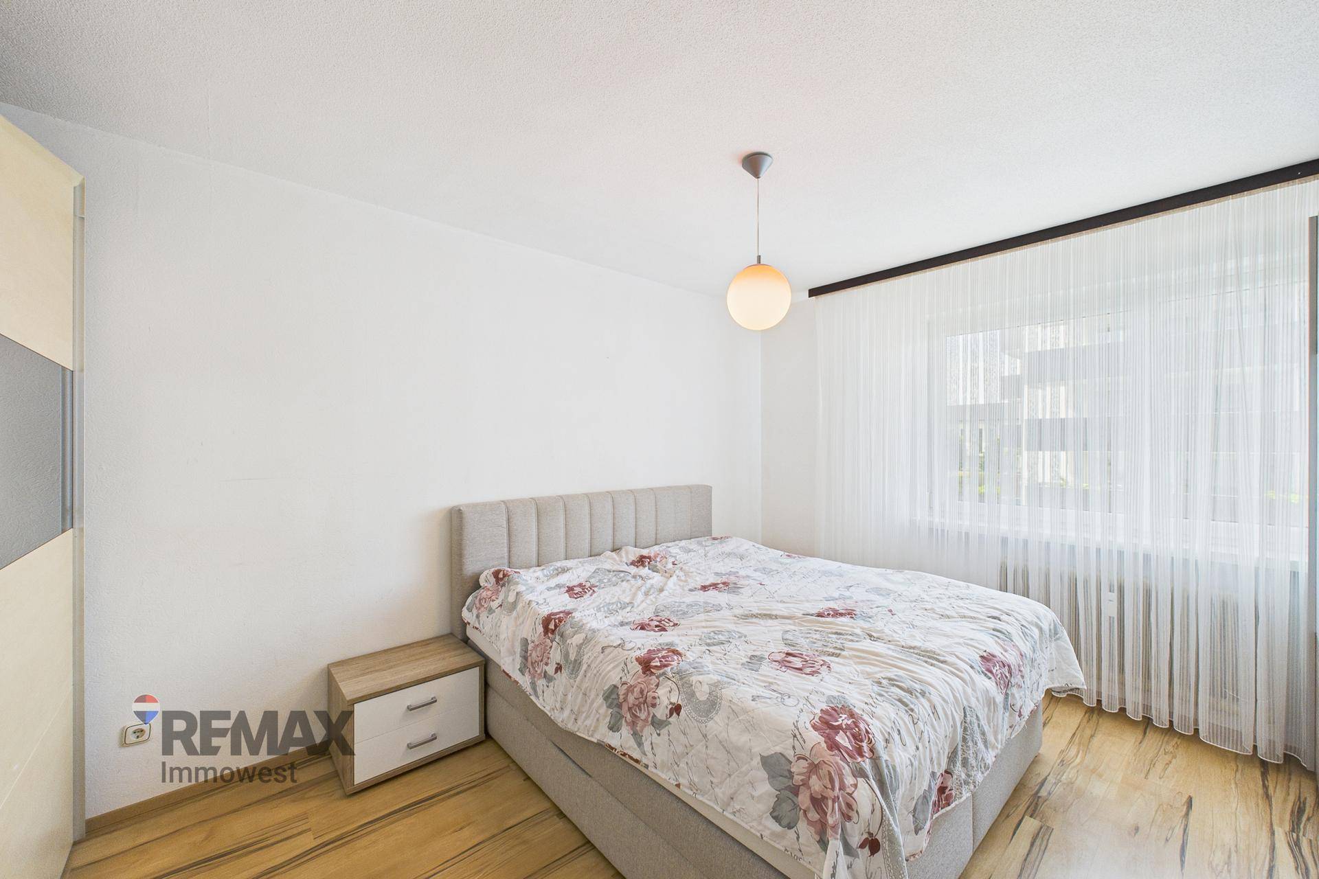 Helles Schlafzimmer mit Doppelbett, Holzboden und großem Fenster mit Vorhängen.