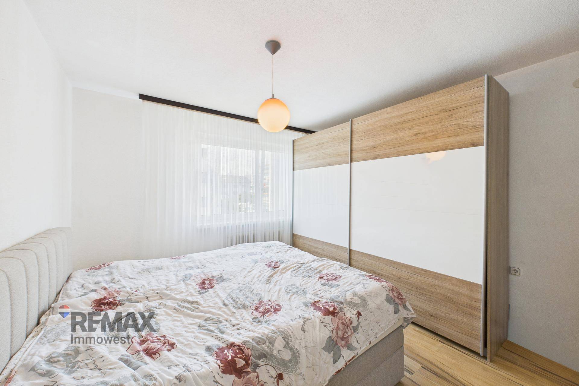 Schlafzimmer mit Doppelbett, Holzboden und großem Schiebetürenschrank in Holz-Weiß-Optik.