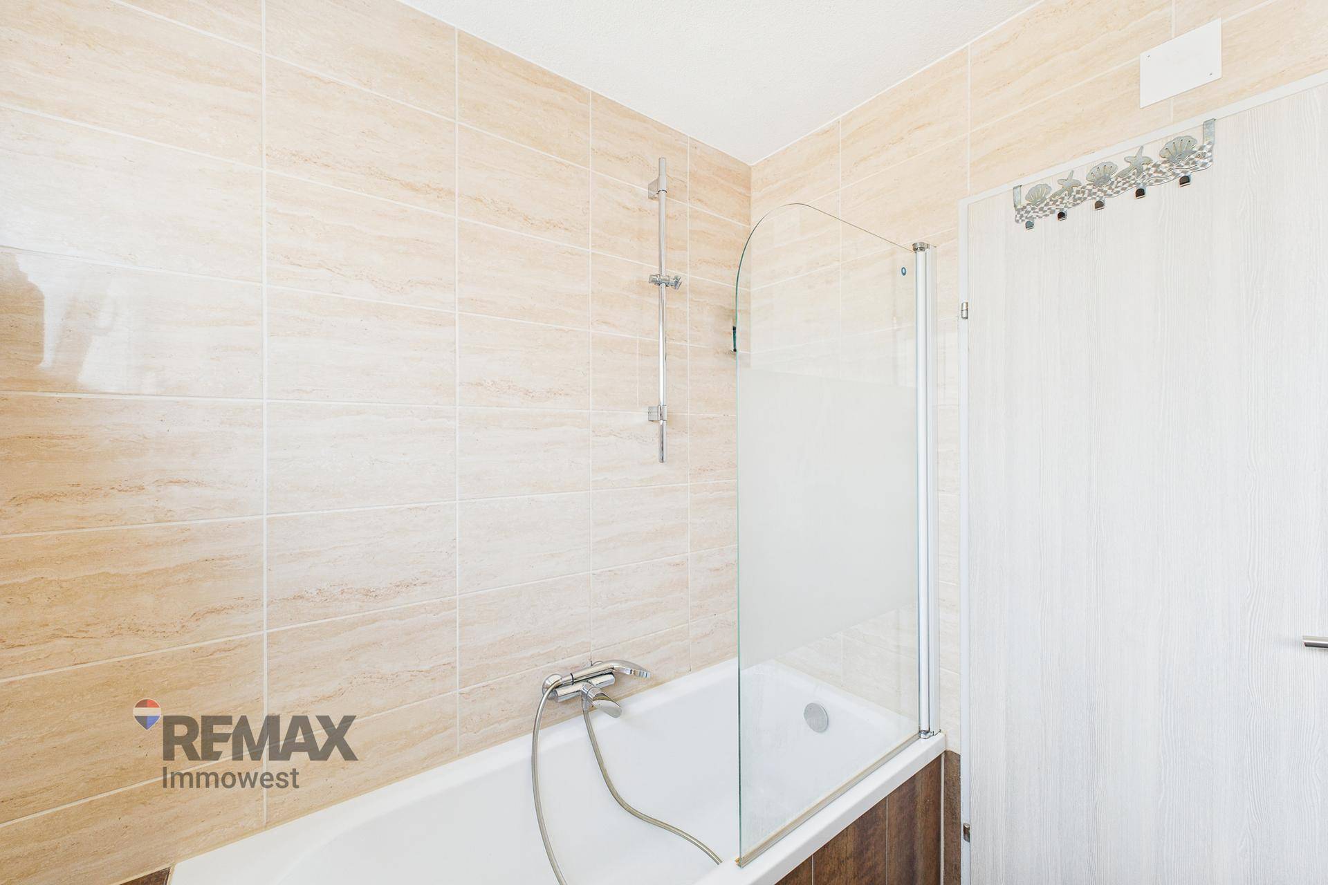 Badezimmer mit Badewanne, Duschabtrennung aus Glas und beigefarbenen Wandfliesen.