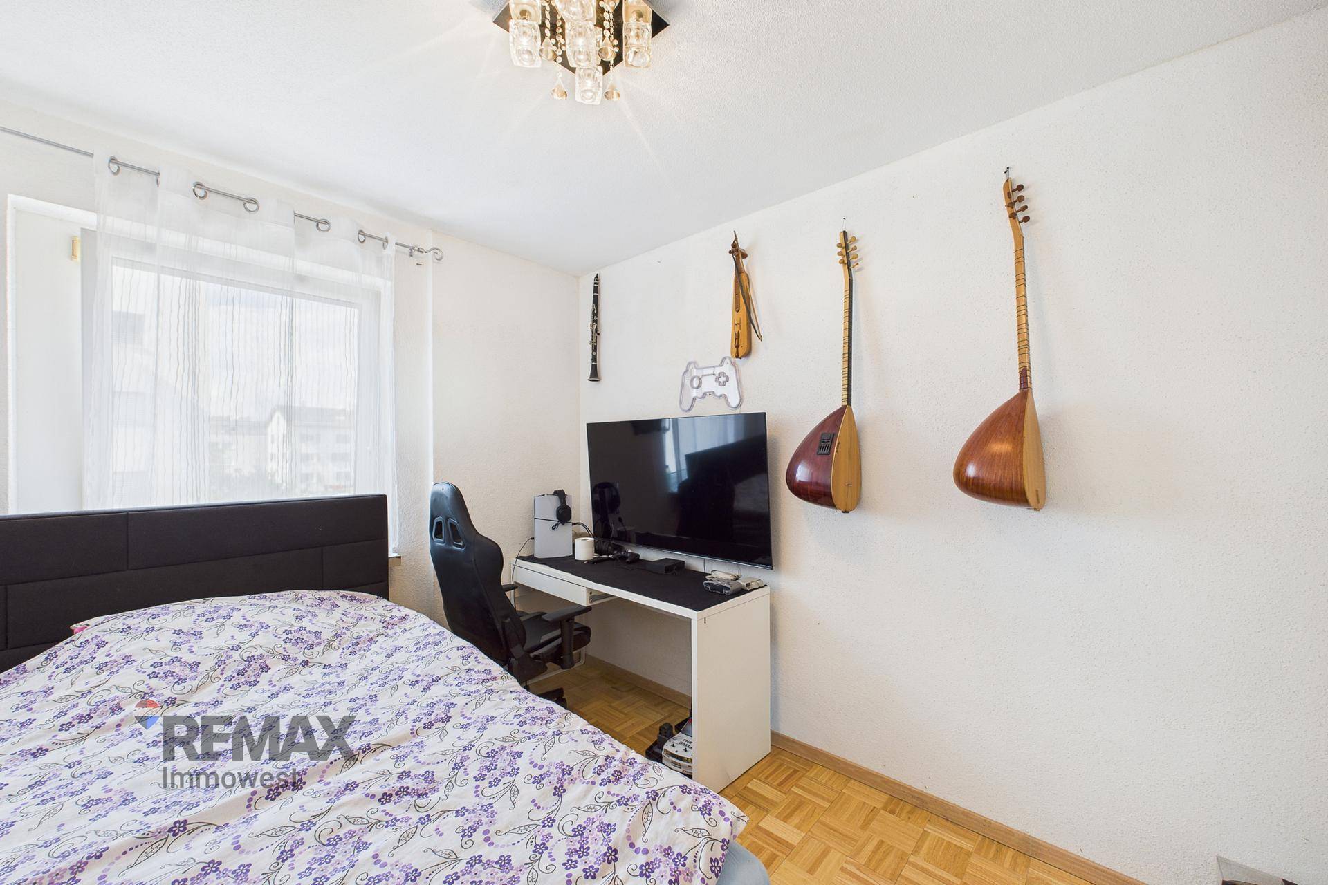 Jugendzimmer mit Bett, Schreibtisch, Gaming-Setup und dekorativen Musikinstrumenten an der Wand.