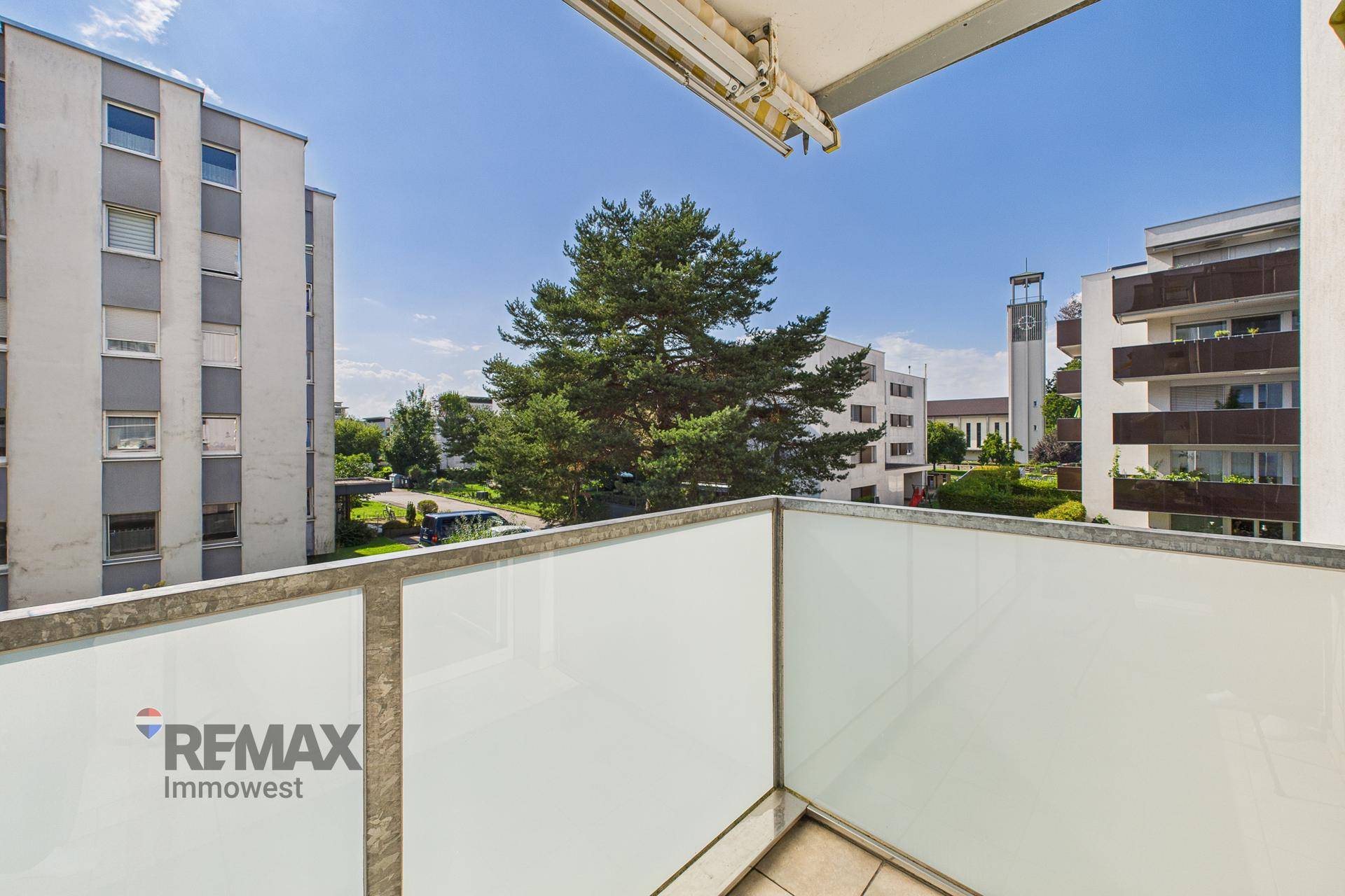 Balkon mit Glasbrüstung und weitem Blick über die Wohnanlage und die Umgebung.