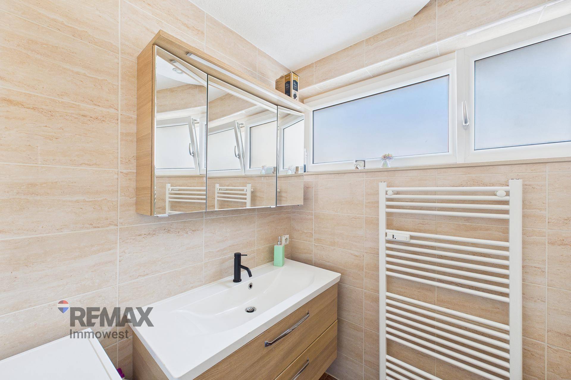 Modernes Badezimmer mit beigefarbenen Fliesen, Waschtisch und Spiegelschrank über dem Waschbecken.
