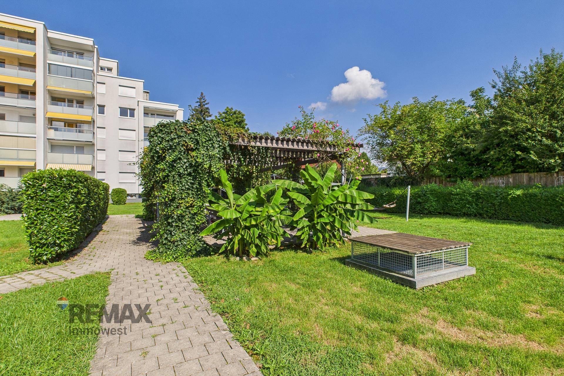 Gepflegte Grünanlage mit Wegen, Bepflanzung und einer überdachten Pergola im Freien.