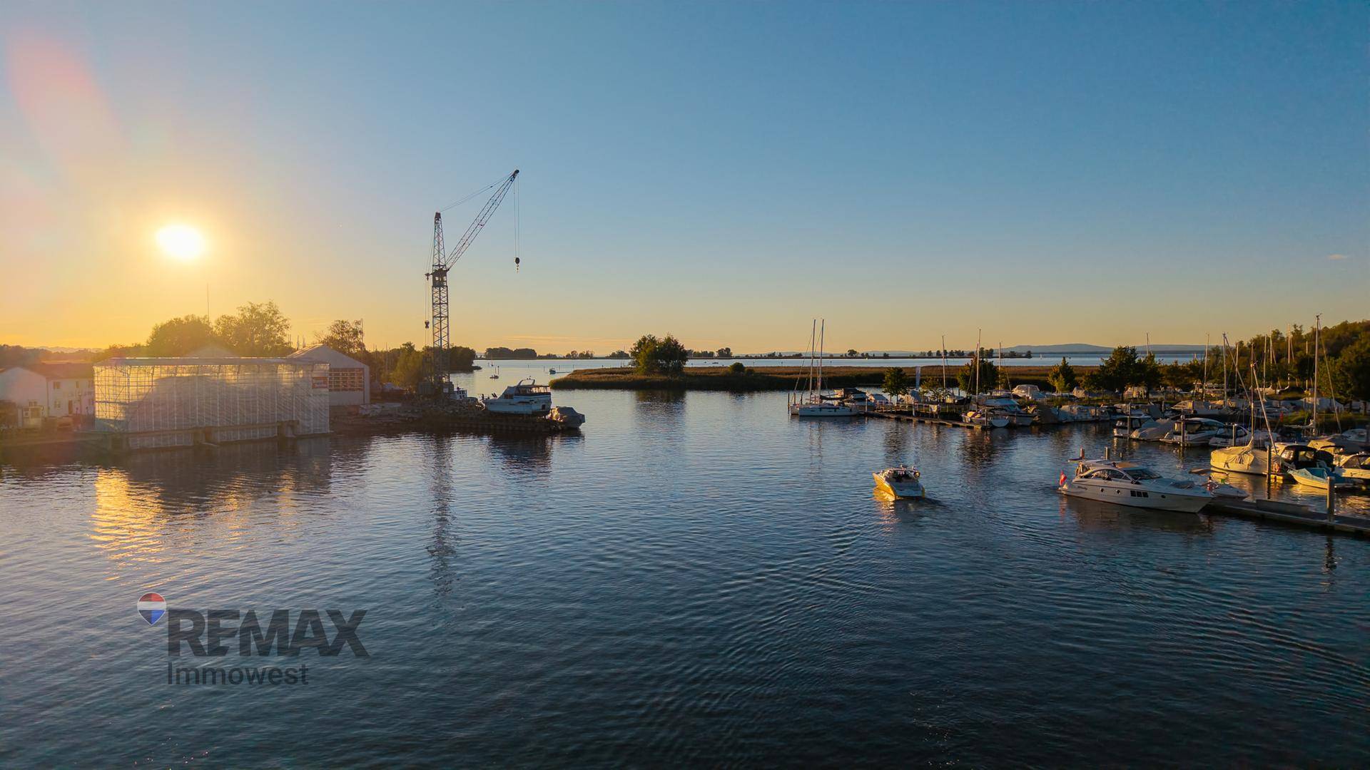 Malerischer Sonnenuntergang über einem Hafen mit zahlreichen Booten und einem Kran.