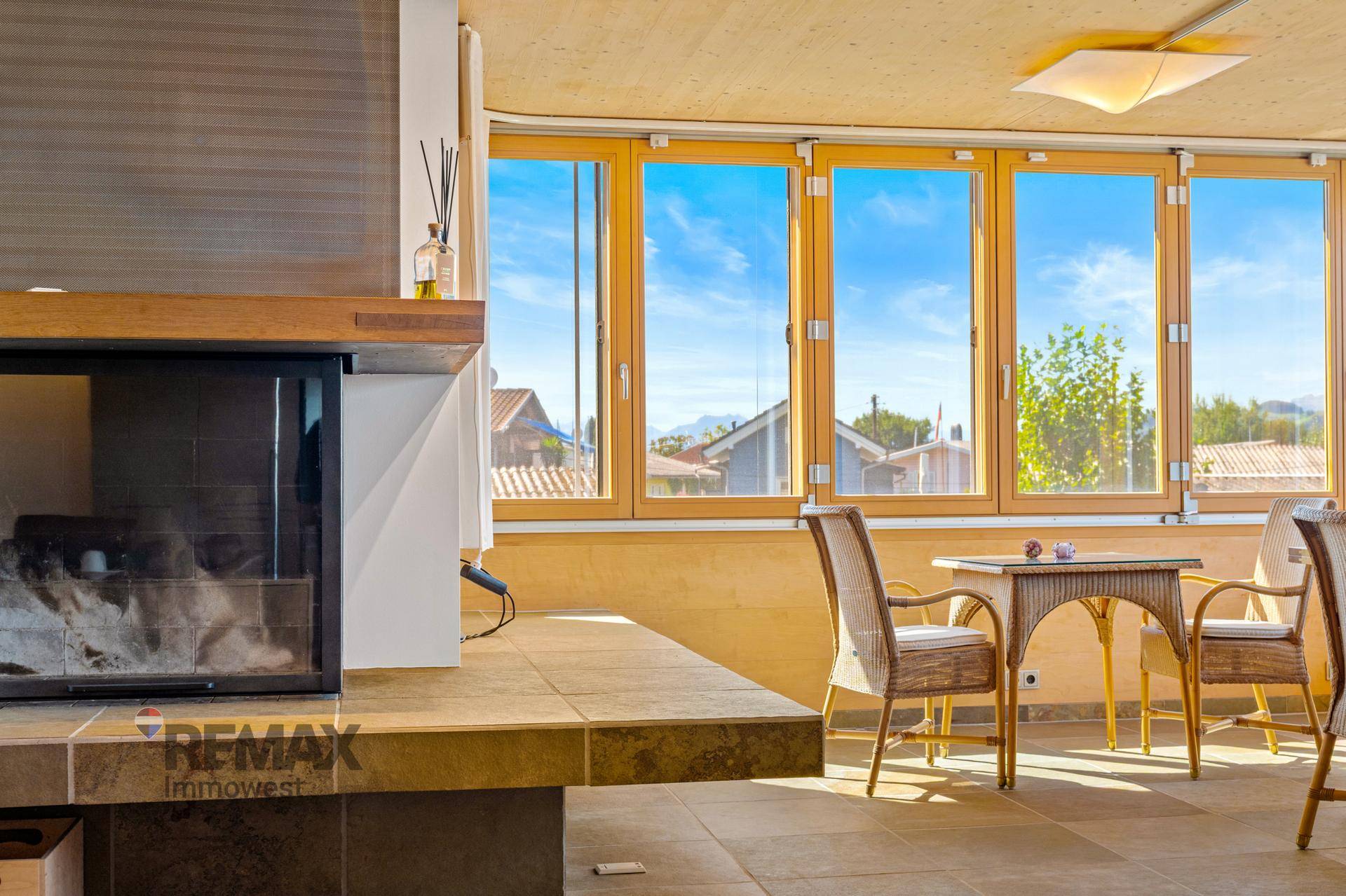 Heller Wintergarten mit Kamin, Rattanmöbeln und weitem Blick auf die Landschaft.