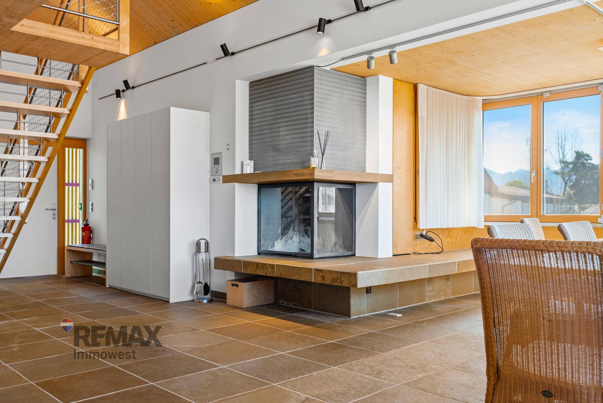 Geräumiges Wohnzimmer mit modernem Kamin, Holztreppe und Fliesenboden.