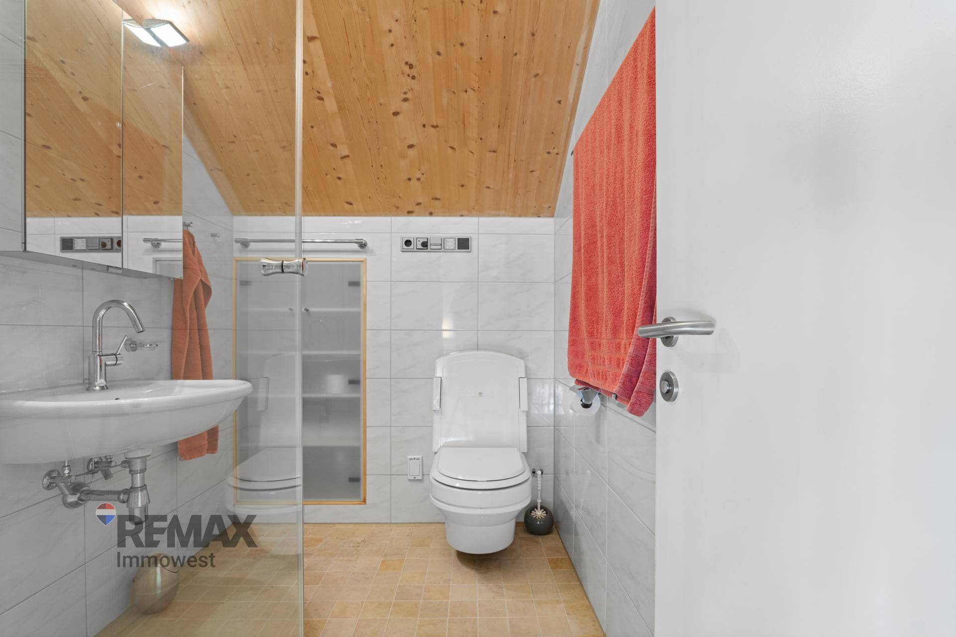 Helles Badezimmer mit WC, Waschbecken, Spiegelschrank und weißen Fliesen.