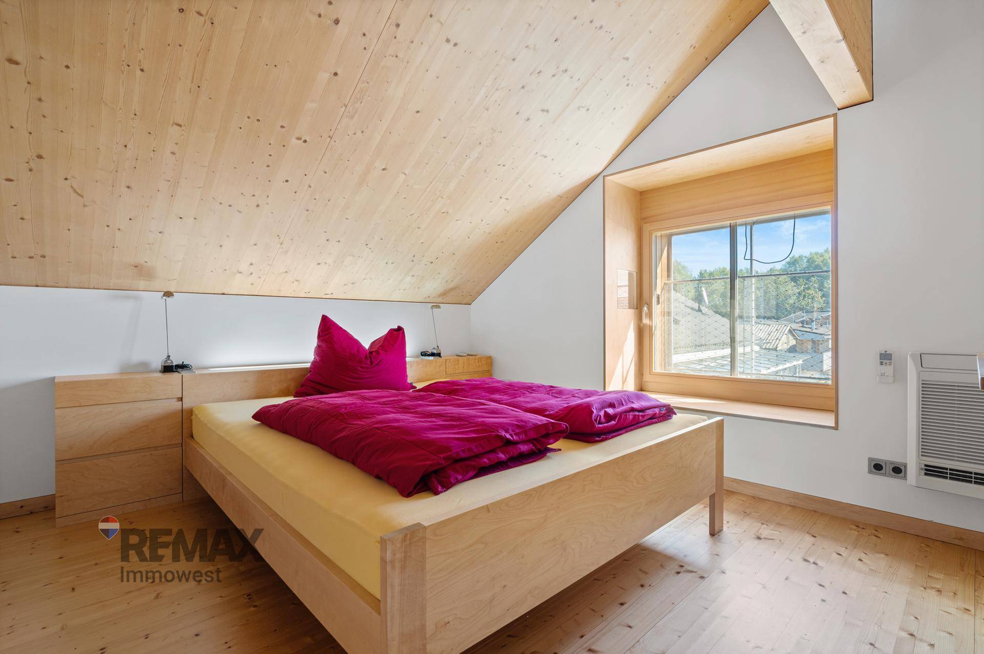 Gemütliches Schlafzimmer mit Holzdachschräge, Holzboden und Fenster mit Ausblick.