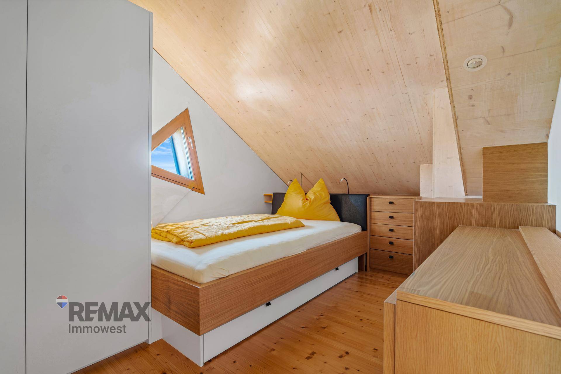 Kinderzimmer mit Holzdachschräge, Einzelbett und dreieckigem Dachfenster.