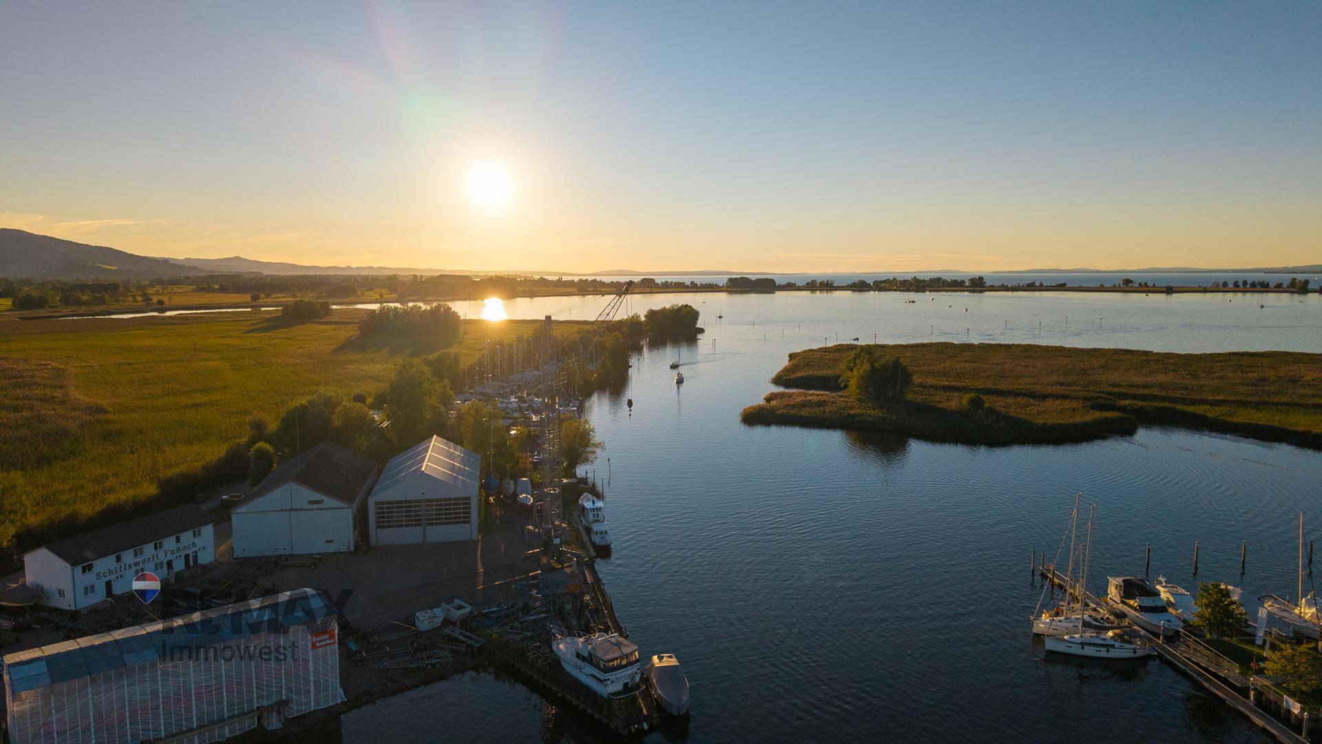 Weitläufige Luftaufnahme eines Sees mit Hafen, Schilf und Sonnenuntergang.