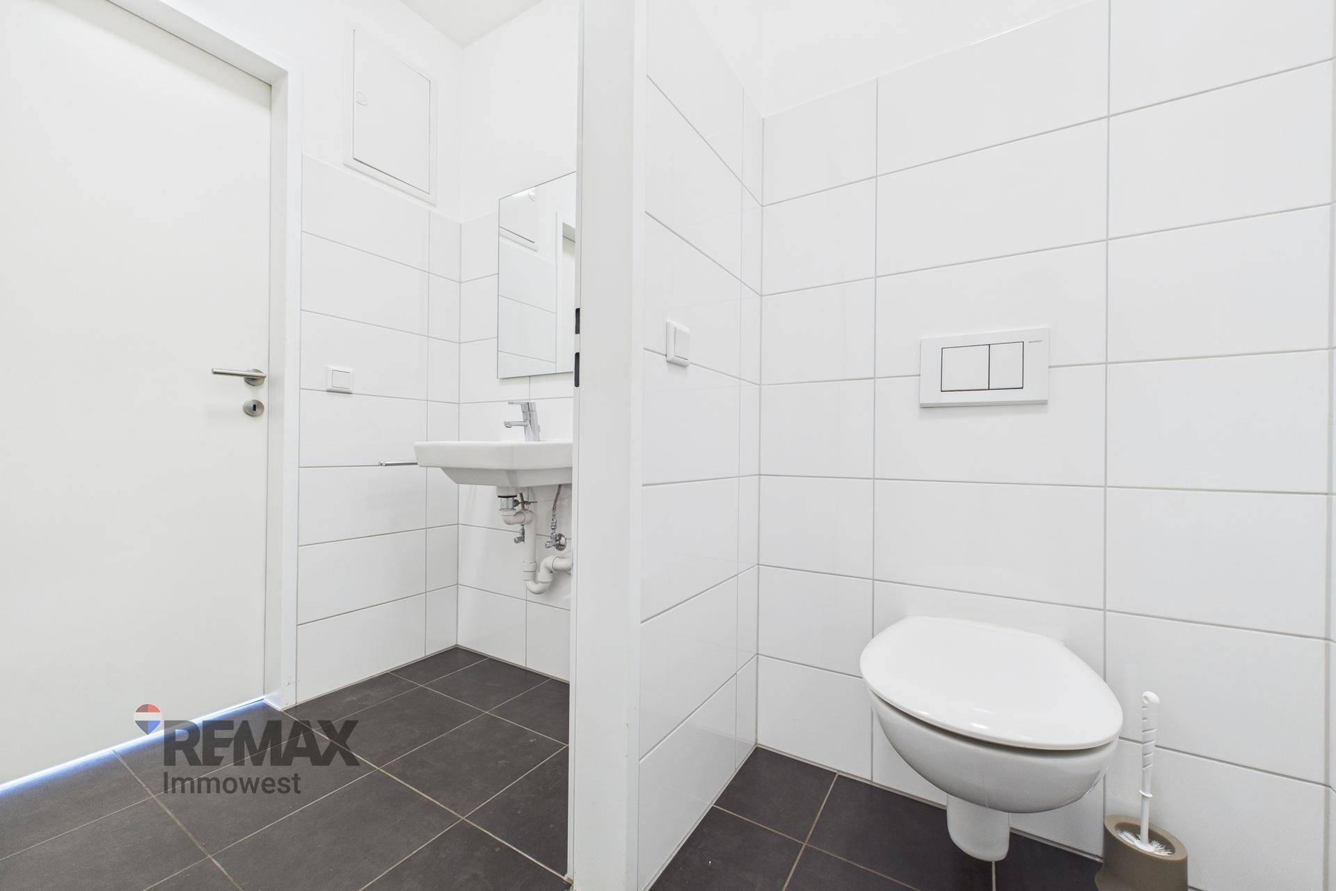 Modernes Gäste-WC mit weißen Fliesen, dunklem Boden und wandhängendem WC.