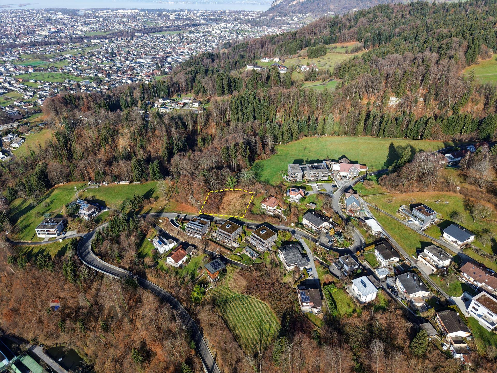 Luftaufnahme eines Baugrundstücks in einer grünen Umgebung mit umliegenden Häusern und Wald.