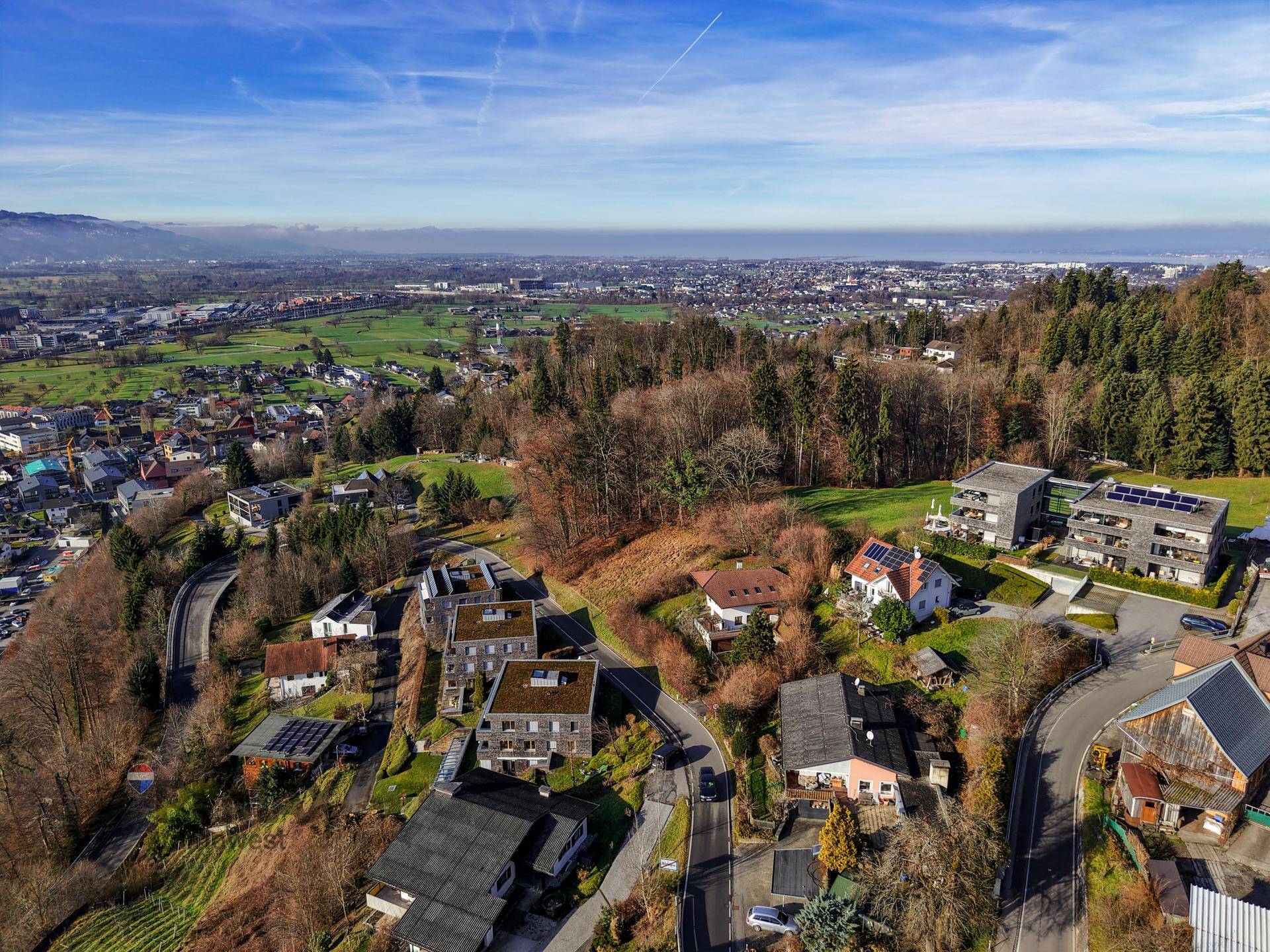 Panoramische Luftaufnahme einer weiten Landschaft mit Stadt, Feldern und schneebedeckten Bergen am Horizont.