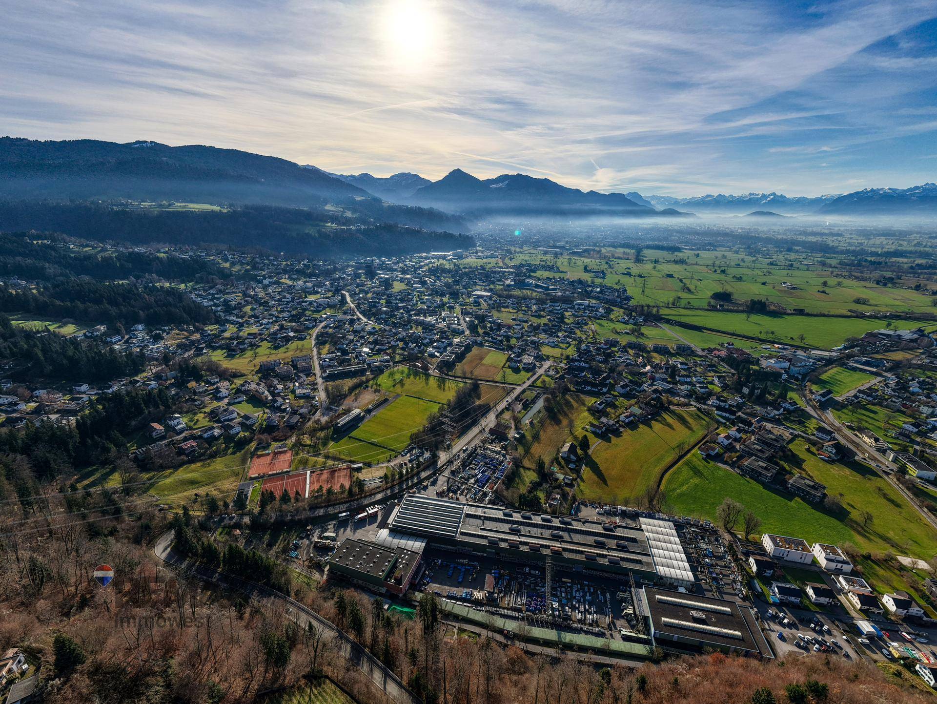 Weitläufige Luftaufnahme eines Tals mit einer Stadt, Industriegebiet, Feldern und Bergen im Hintergrund.
