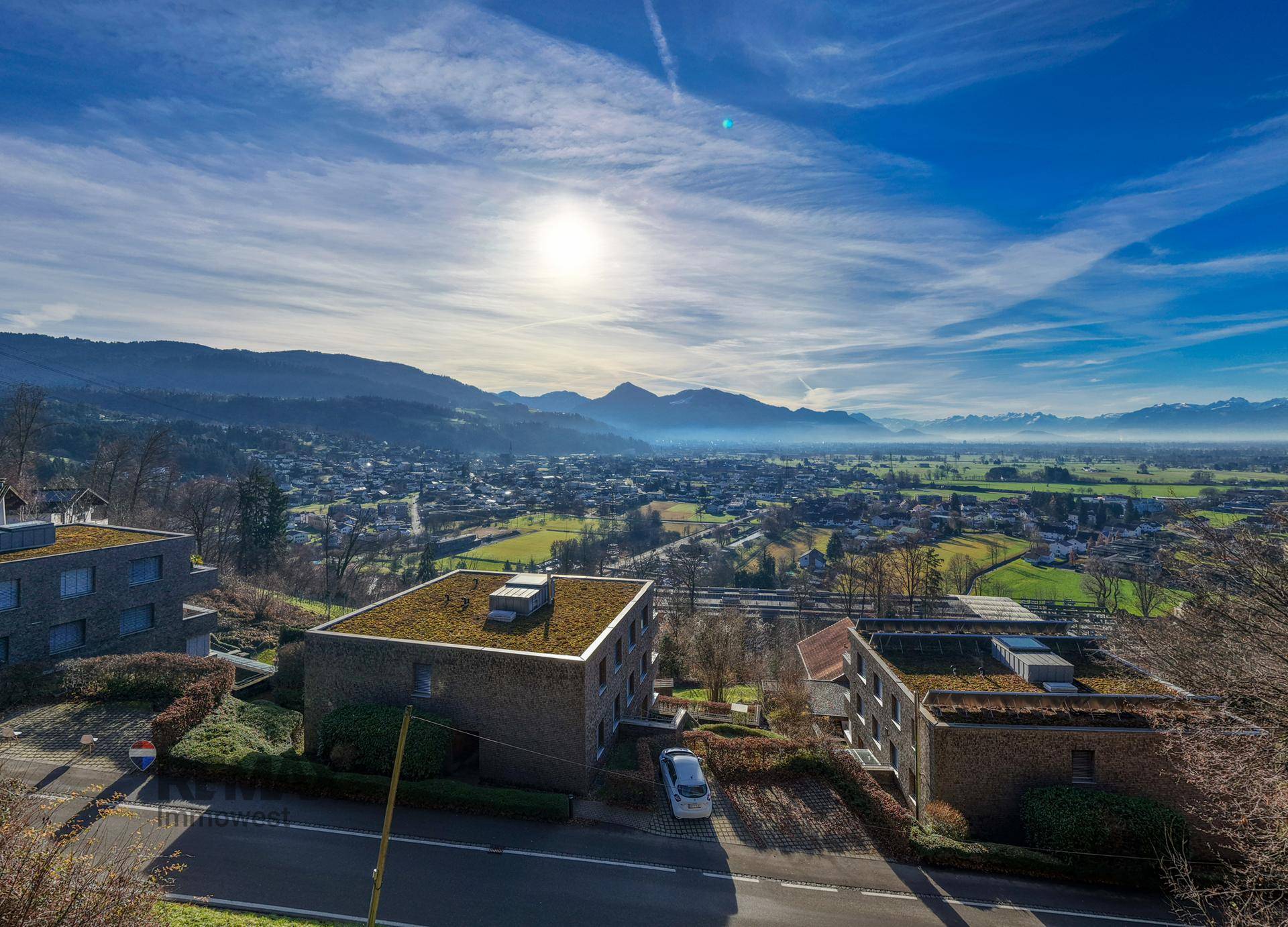 Moderne Gebäude mit Gründächern und Panoramablick über ein Tal mit Bergen unter blauem Himmel.