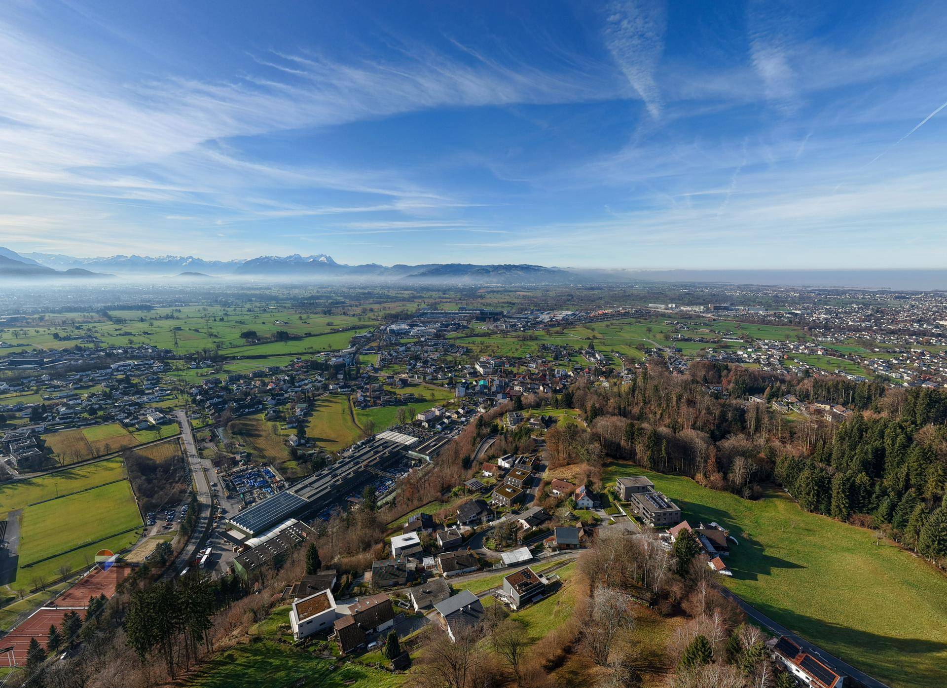Weitläufige Luftaufnahme einer ländlichen Gegend mit Siedlungen, Feldern und einer Bergkette am Horizont.