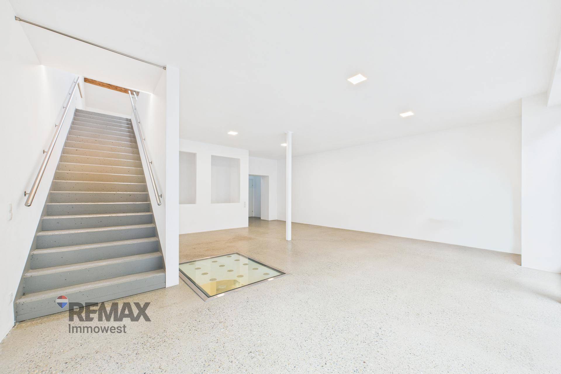 Heller, offener Gewerberaum im Erdgeschoss mit Treppe und einem Glasbodenfenster.