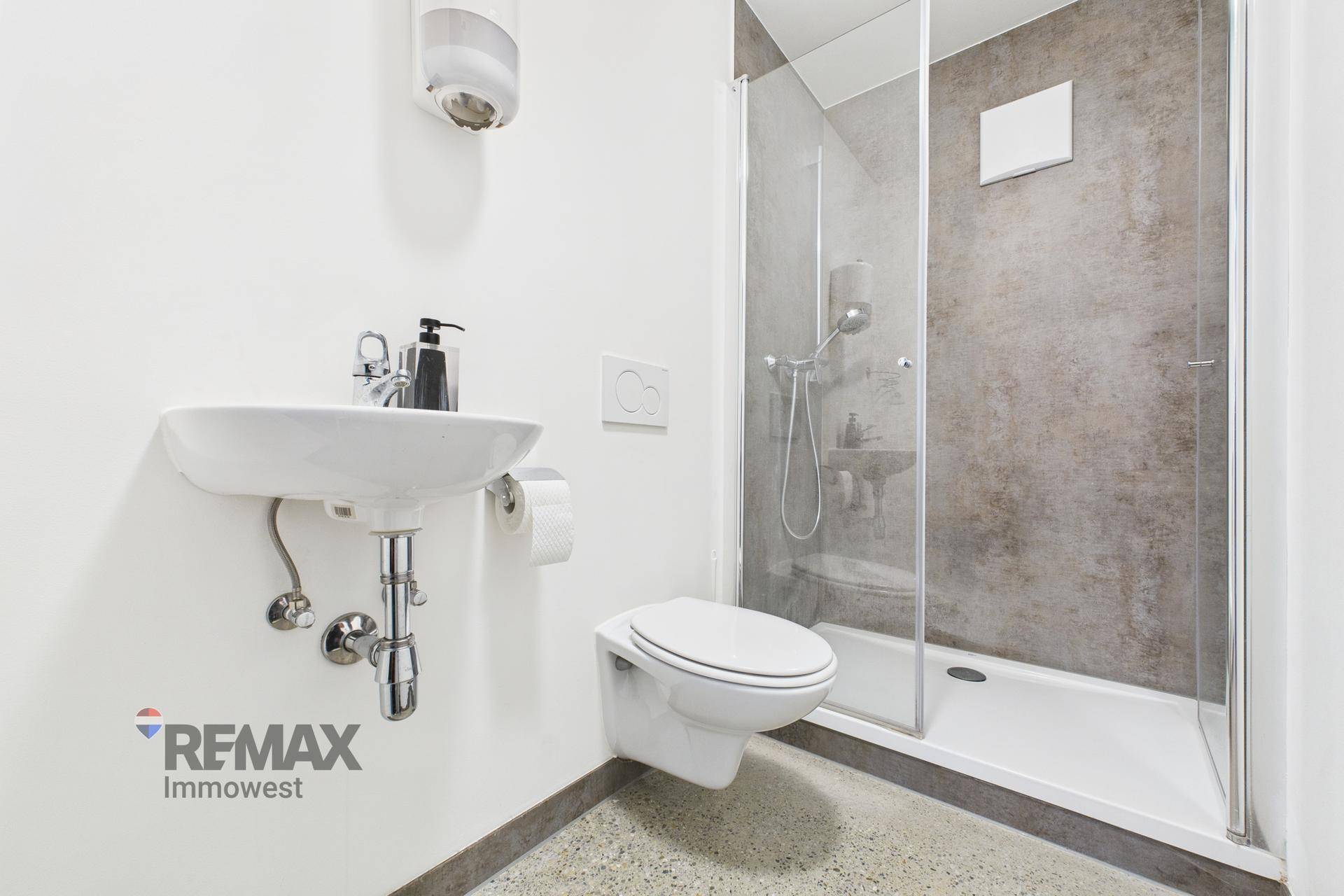 Modernes Badezimmer mit Duschkabine, wandhängendem WC und kleinem Waschbecken.