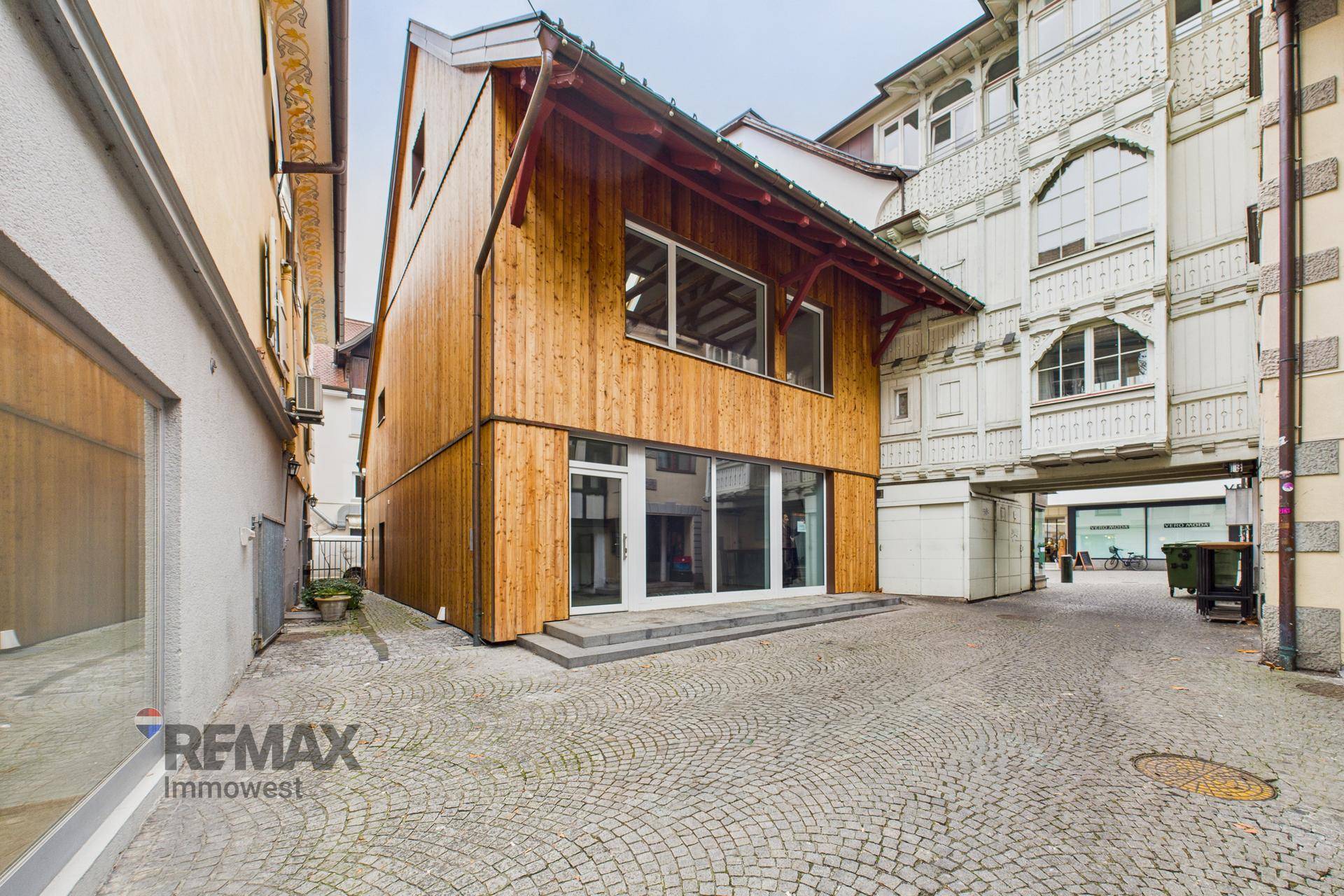 Modernes Gebäude mit Holzfassade und großen Fenstern in einer historischen Gasse.