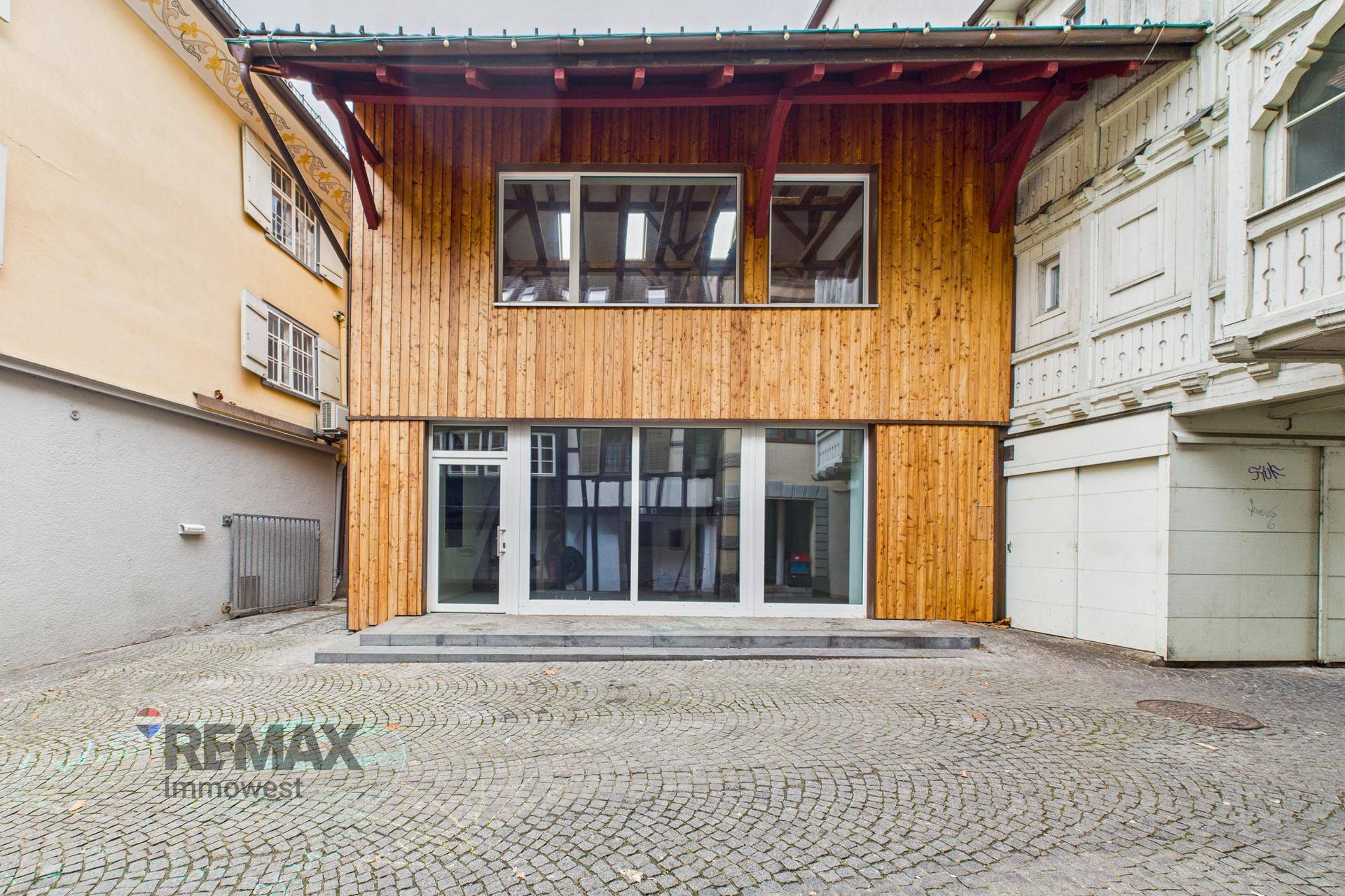 Ansicht der modernen Holzfassade eines Gebäudes mit großen Schaufenstern und Kopfsteinpflaster.