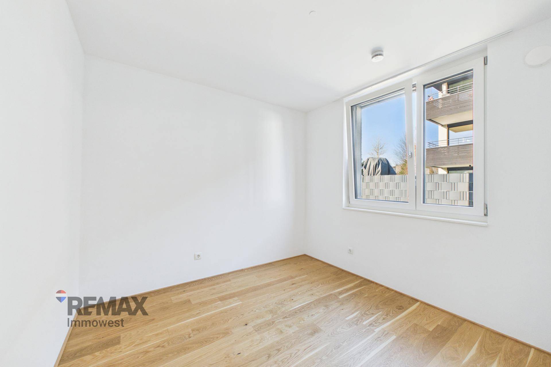 Geräumiges, leeres Zimmer mit Holzboden und großem Fenster für viel Helligkeit.