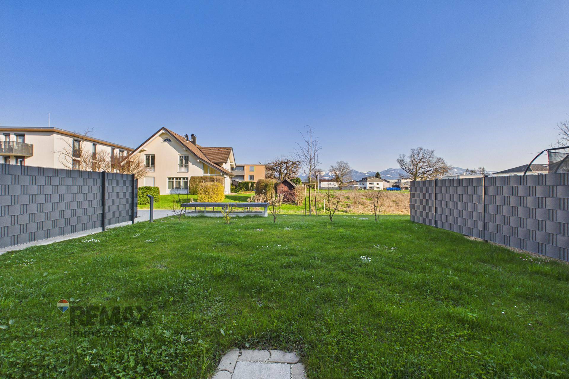 Weitläufiger Garten mit Rasenfläche und Zaun, umgeben von Wohngebäuden.