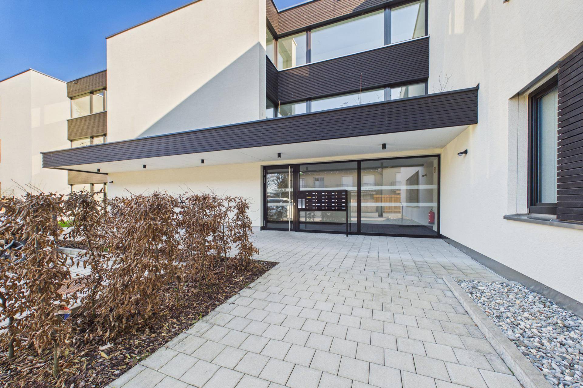 Moderner Eingangsbereich eines Mehrfamilienhauses mit gepflastertem Weg.
