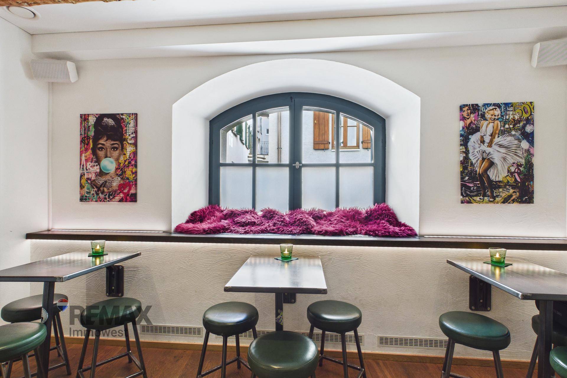 Sitzbereich mit kleinen Tischen und Hockern, einem Bogenfenster und Pop-Art an den Wänden.