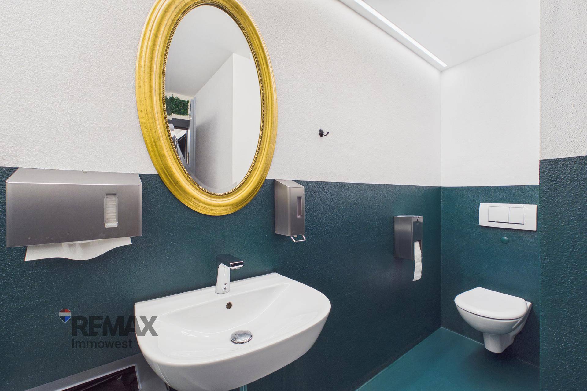 Gästetoilette mit Waschbecken, Wand-WC und einem ovalen Spiegel in goldenem Rahmen.