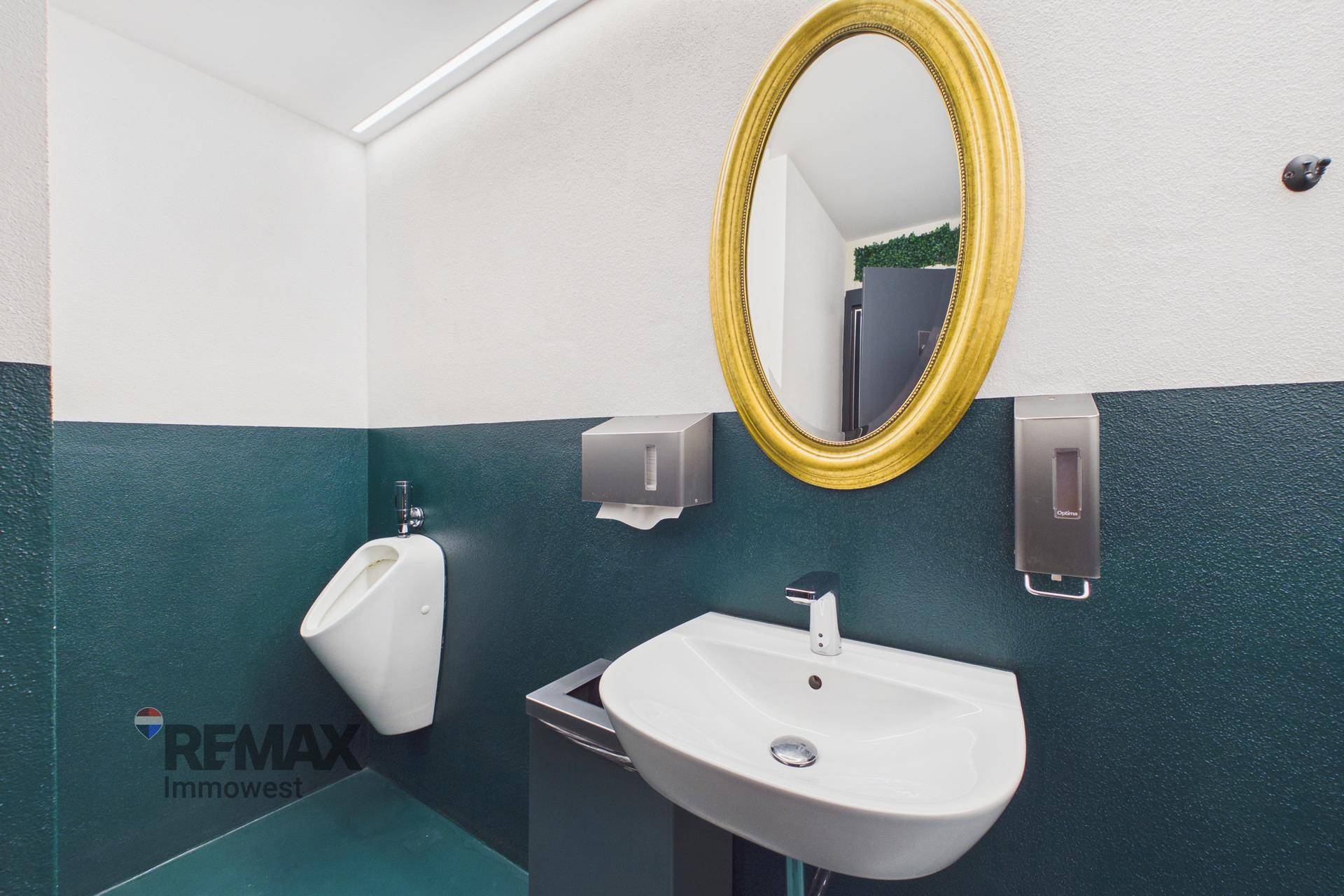 Gästetoilette mit Waschbecken, Urinal und einem ovalen Spiegel in goldenem Rahmen.