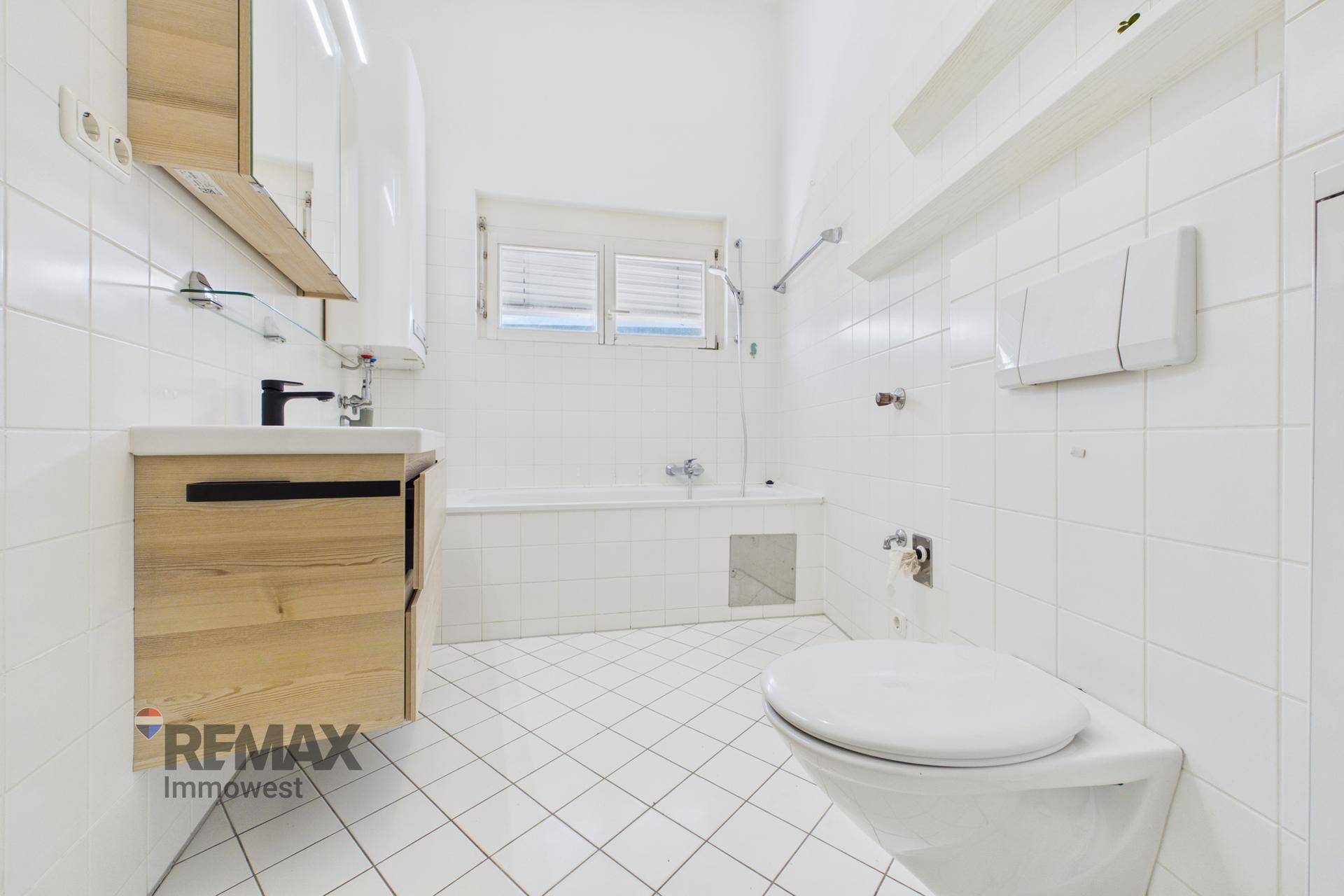 Gefliestes Badezimmer mit Badewanne, WC, Waschbecken und Fenster.