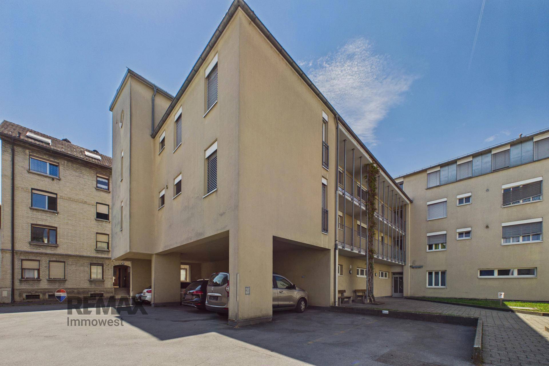 Gebäudeseite mit überdachten Parkplätzen und angrenzendem Grünbereich.