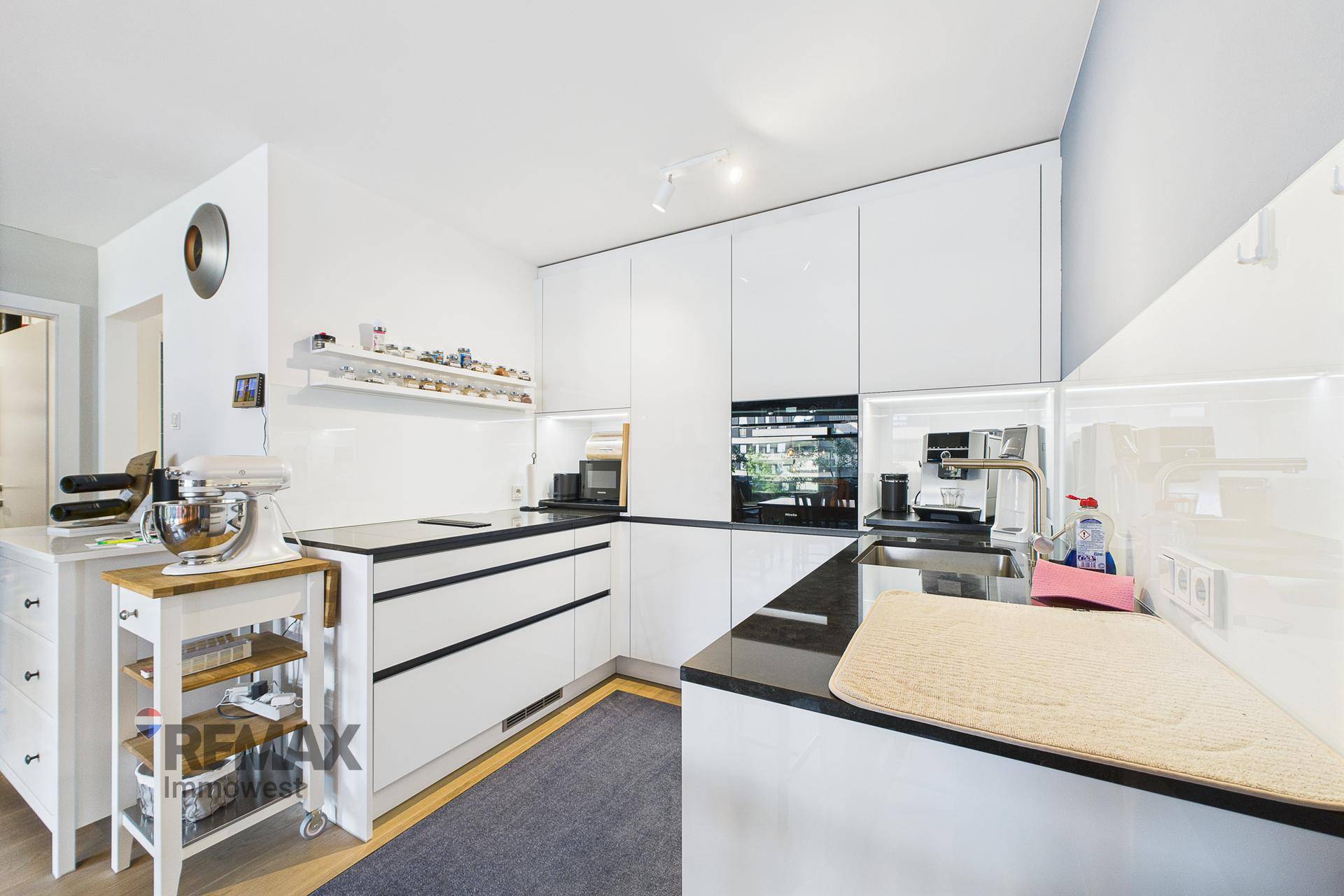 Moderne, weiße Einbauküche mit Hochglanzfronten und dunkler Arbeitsplatte.