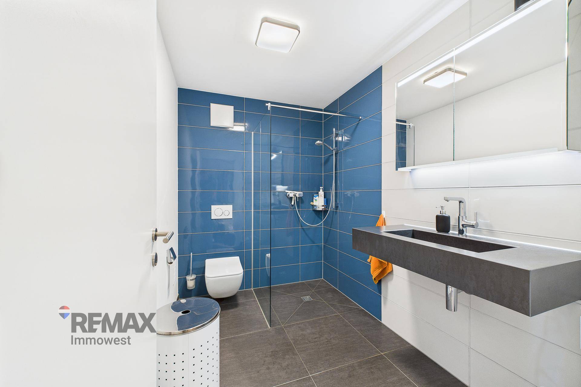 Modernes Badezimmer mit blauen Wandfliesen, begehbarer Dusche und Hänge-WC.