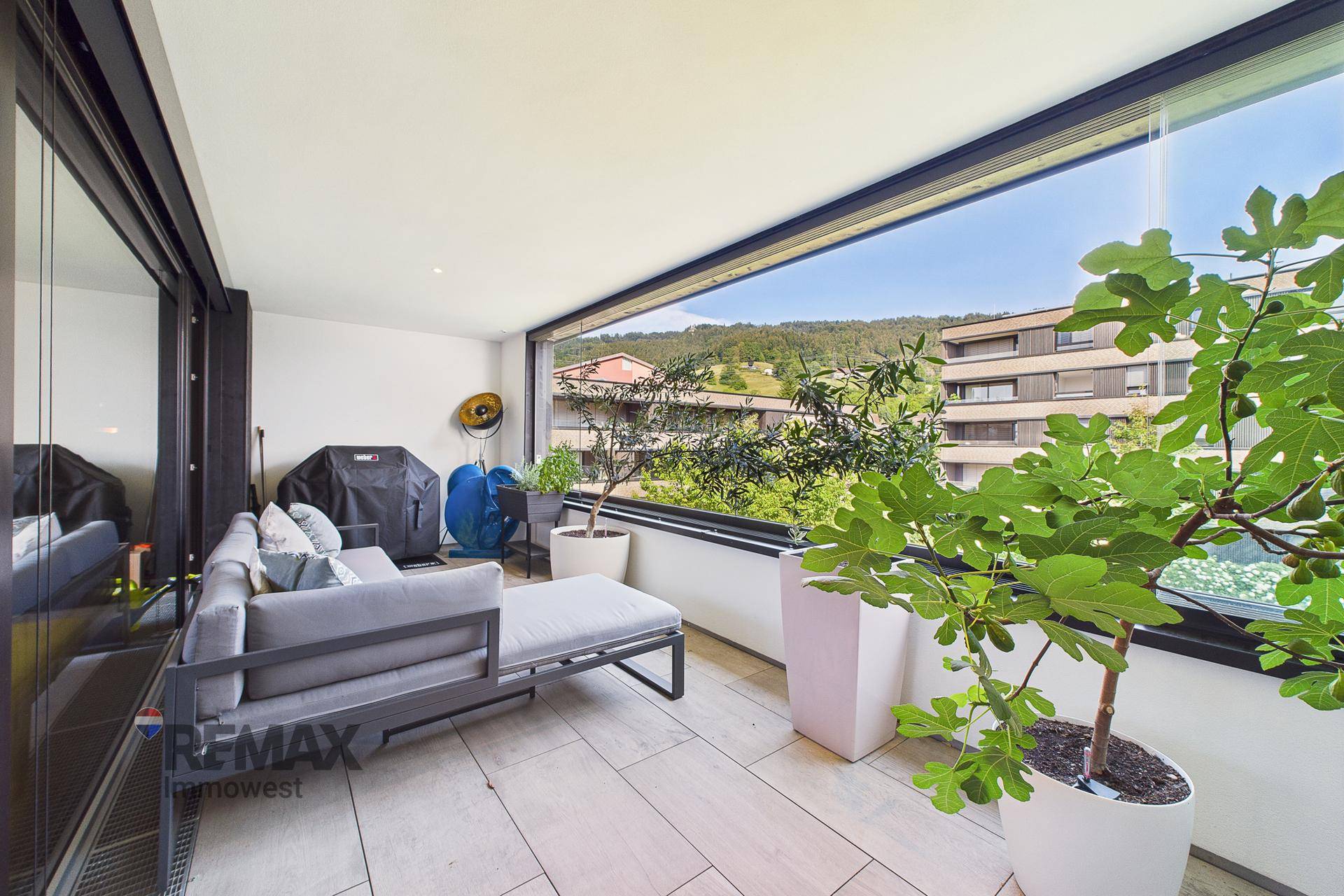 Geräumiger, verglaster Balkon mit Loungemöbeln und weitem Blick ins Grüne.