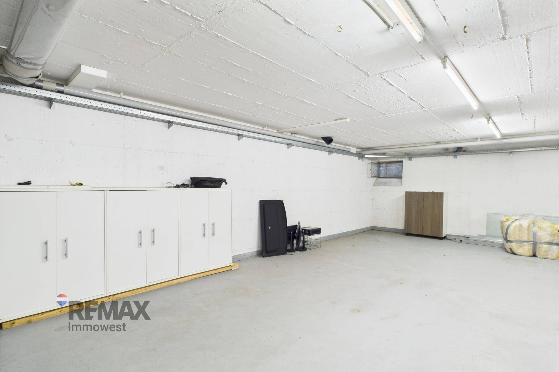 Geräumiger Kellerraum mit Betonboden, weißen Wänden und sichtbaren Installationen an der Decke.