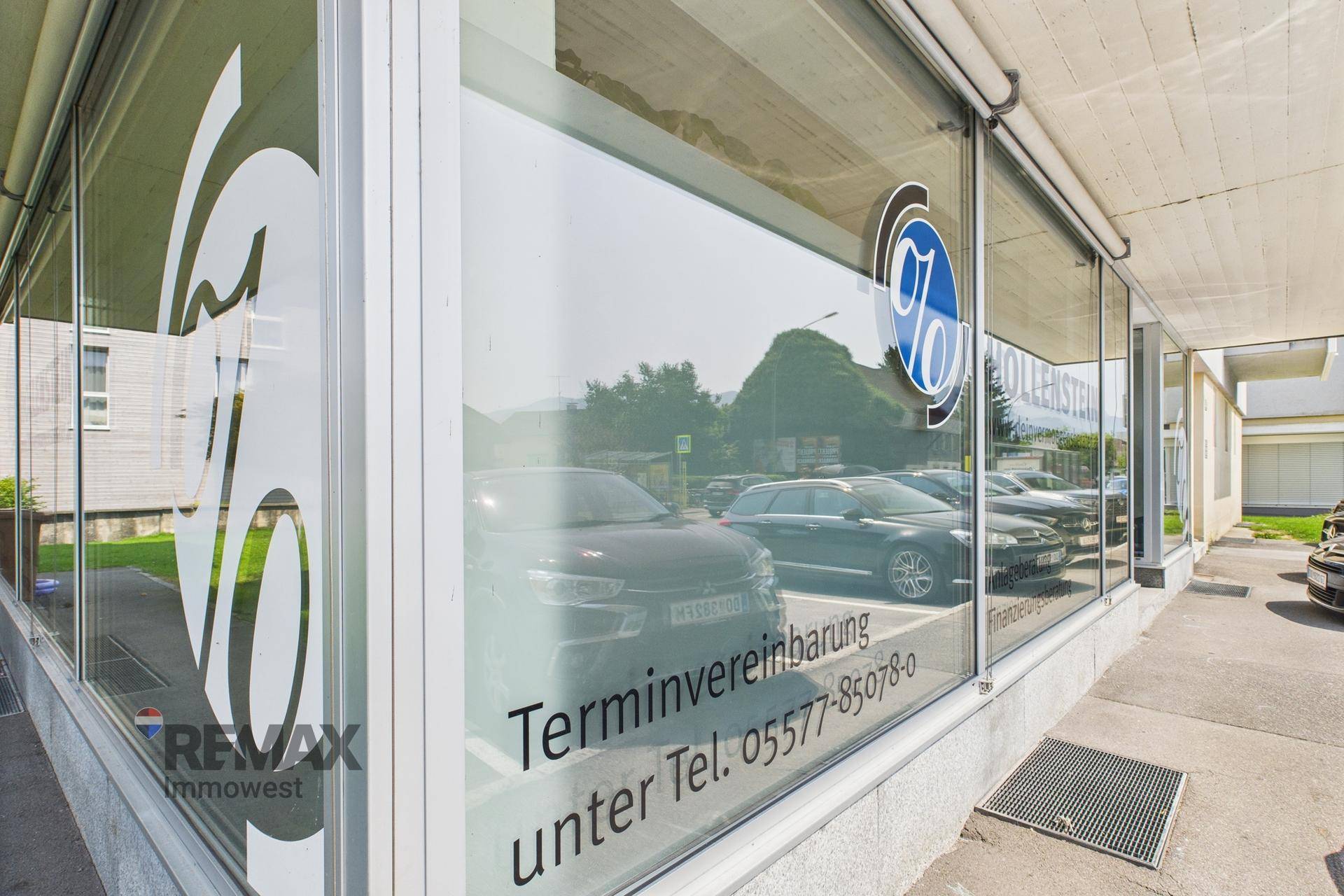 Moderne Glasfassade eines Geschäftsgebäudes mit reflektierenden Fenstern und Werbeaufschrift.